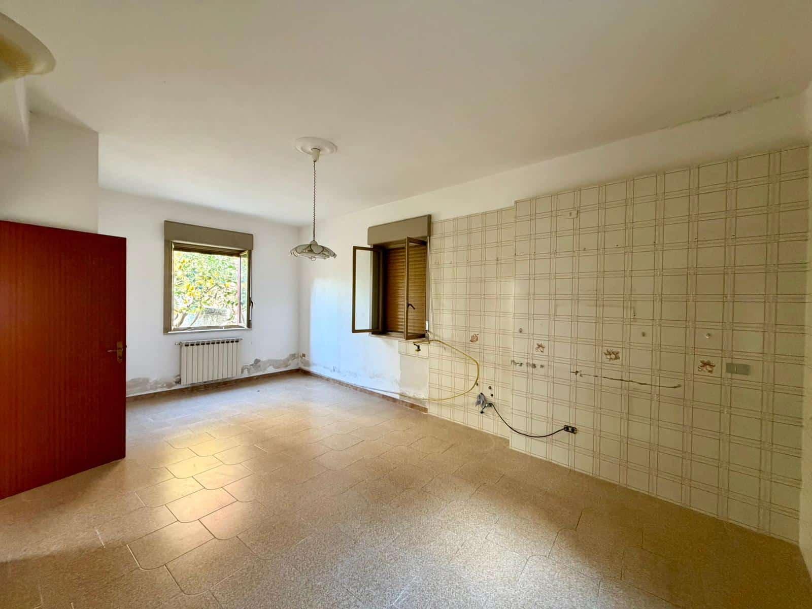 Interno di una stanza vuota con pareti bianche, finestra e pavimento in piastrelle, pronta per ristrutturazione o arredamento.
