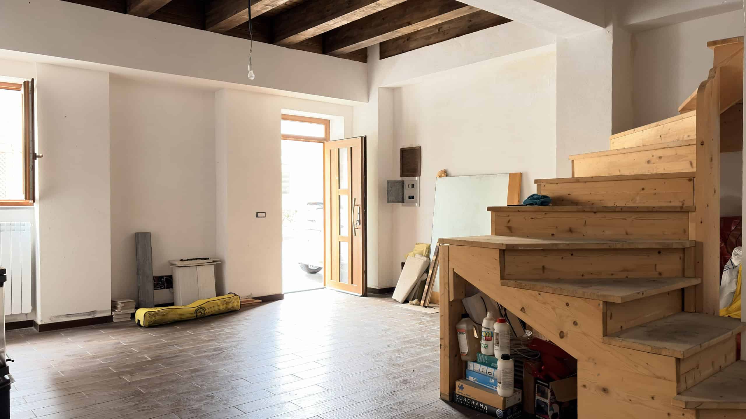 Pannello di ingresso di una casa moderna con scala in legno, spazio luminoso e arredamento minimalista, pronto per essere personalizzato o ristrutturato.