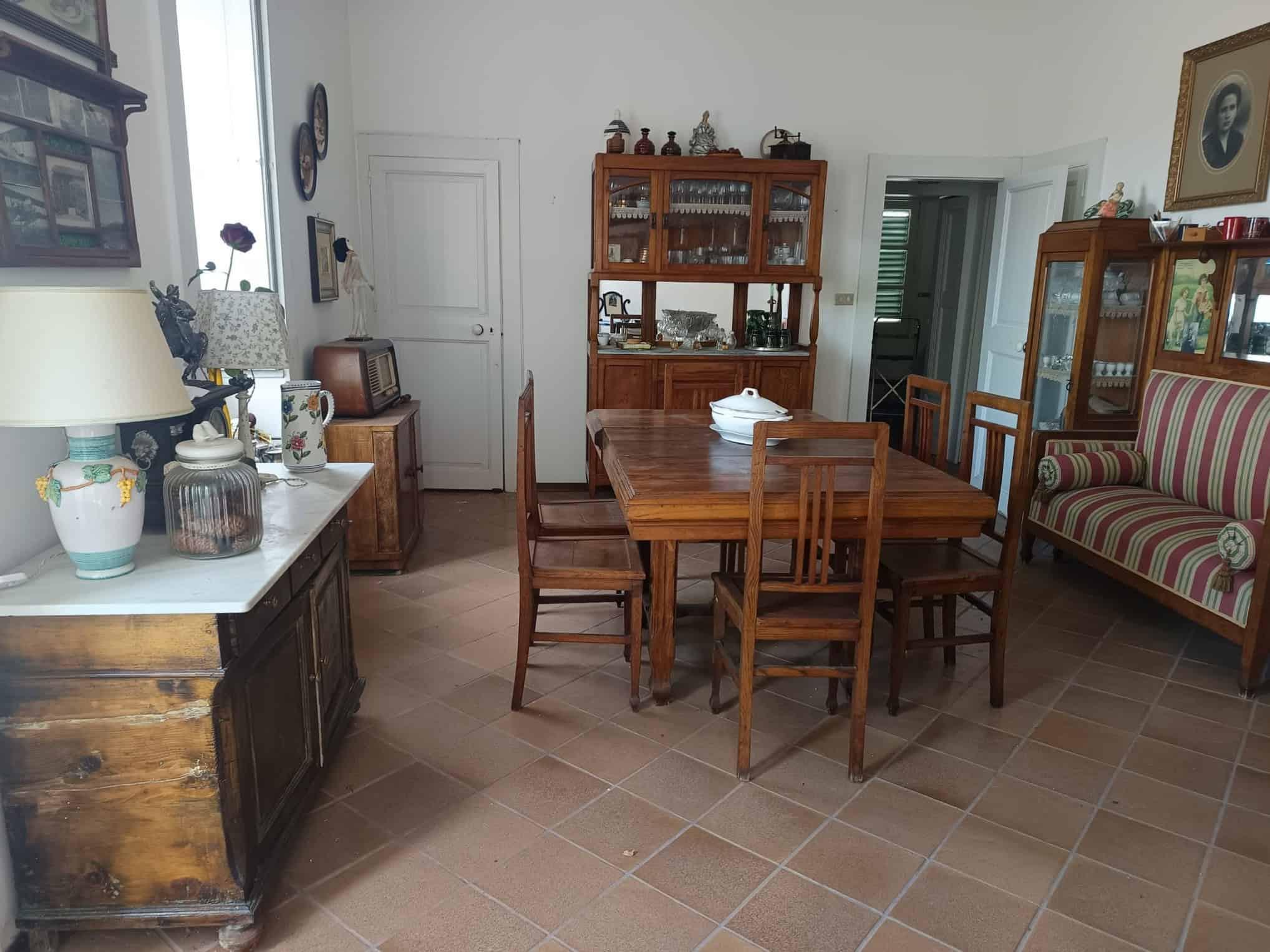 Una sala da pranzo classica con tavolo in legno e sedie, arredamento vintage e oggetti decorativi, ambiente luminoso e accogliente, ideale per convivialità e momenti di relax in famiglia.