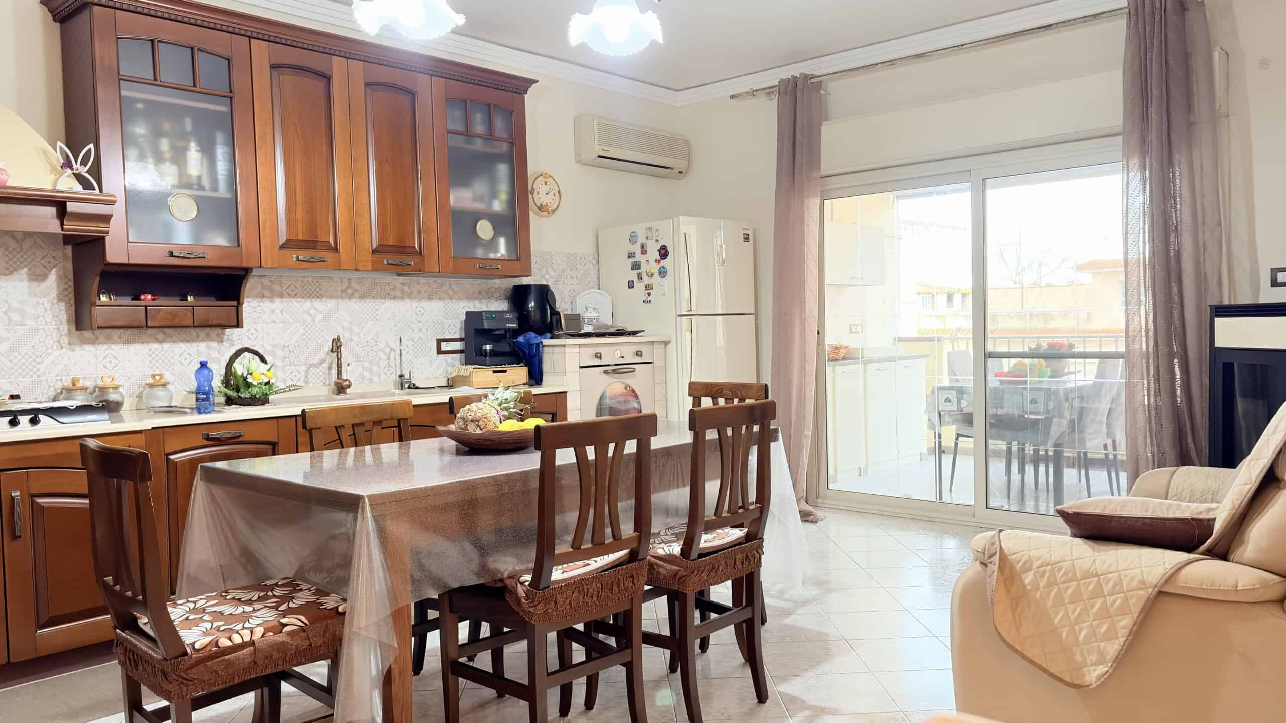 Ampia cucina soggiorno con tavolo da pranzo, mobili in legno e accessori moderni, ambiente luminoso con balcone e vista esterna, ideale per vivere momenti conviviali e pratici.
