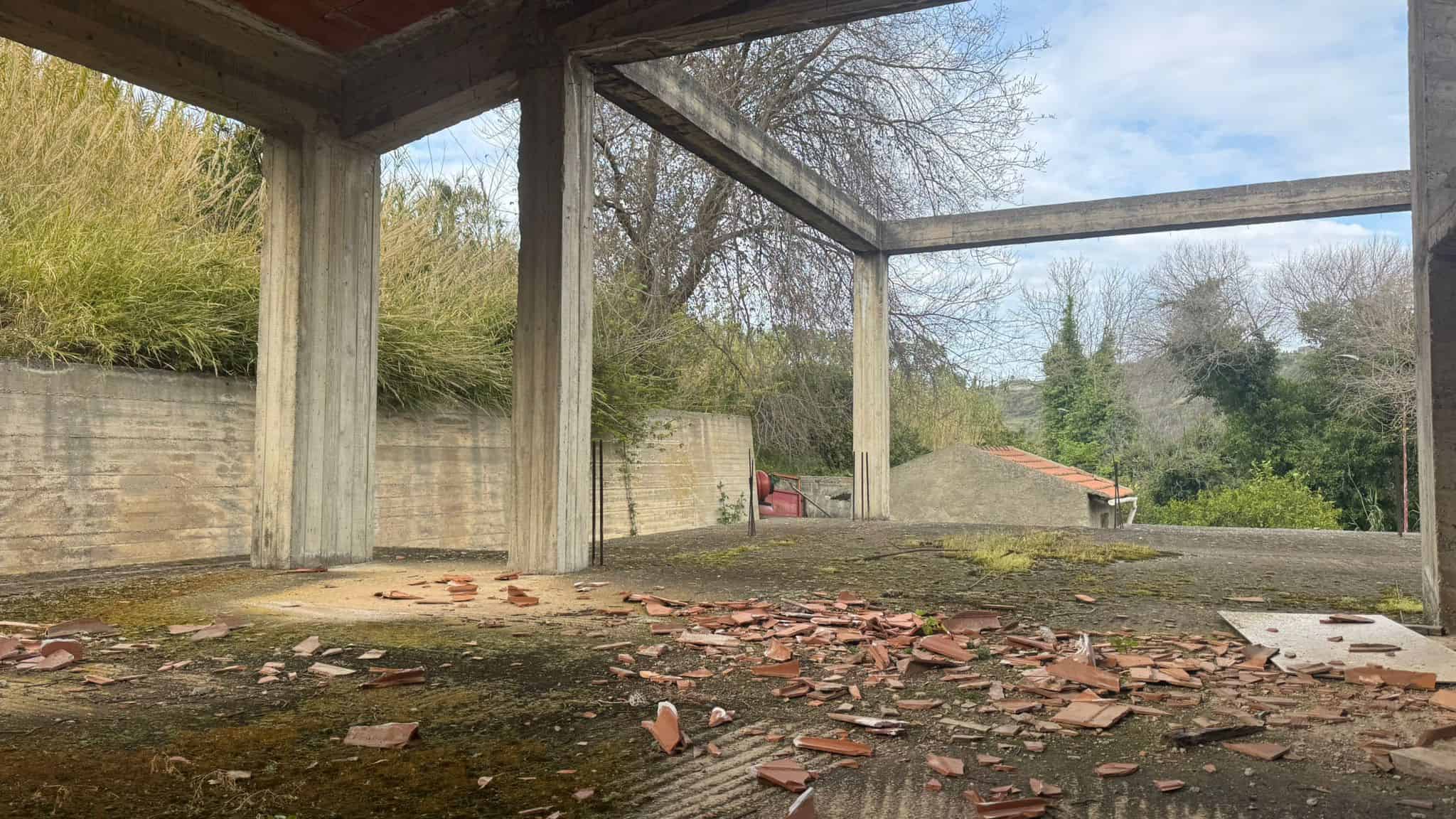 Scorcio di un edificio in costruzione con struttura in cemento e pareti in mattoni rossi, circondato da natura verde e cielo sereno, pronto per essere completato.