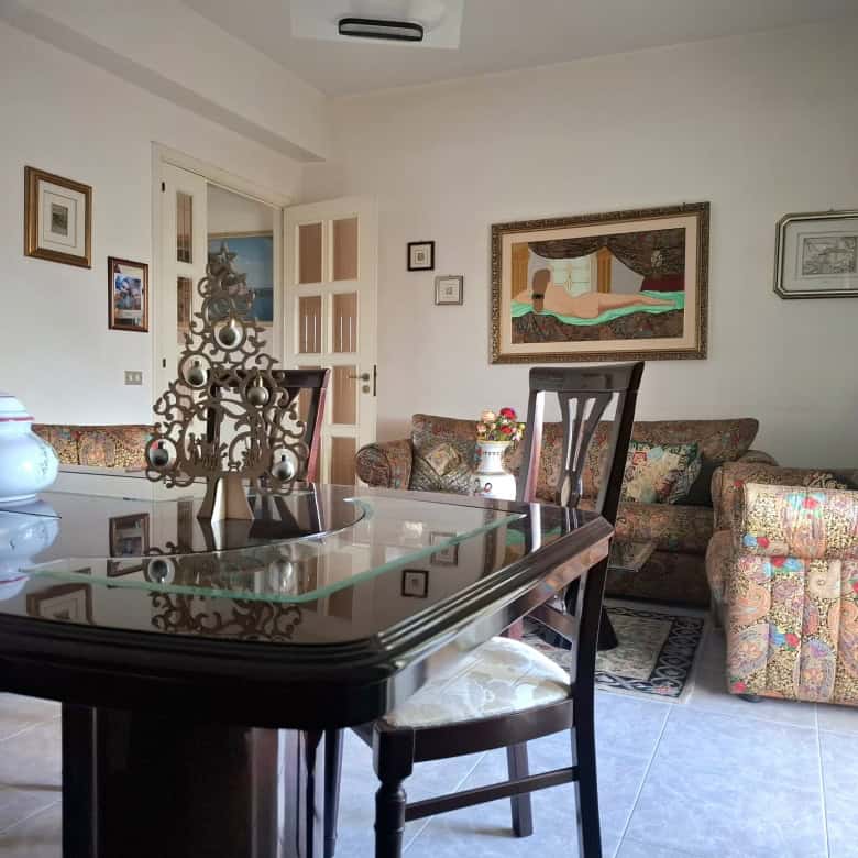 L'immagine mostra un soggiorno accogliente con mobili classici, pareti decorate con quadri e un tavolo in legno con sedie, creando un ambiente elegante e confortevole.
