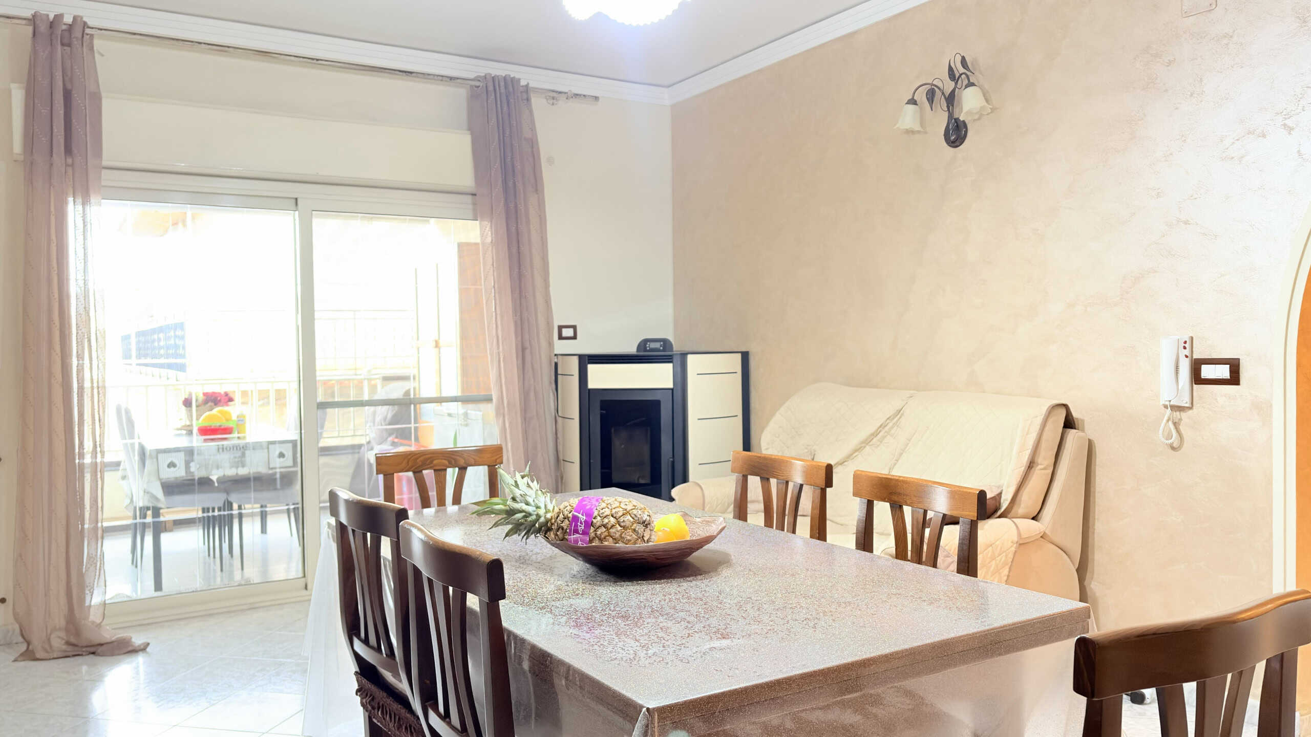 Ampia sala da pranzo con tavolo in marmo, sedie in legno, divano beige e balcone con vista su area esterna, ideale per vivere momenti di convivialità e relax.