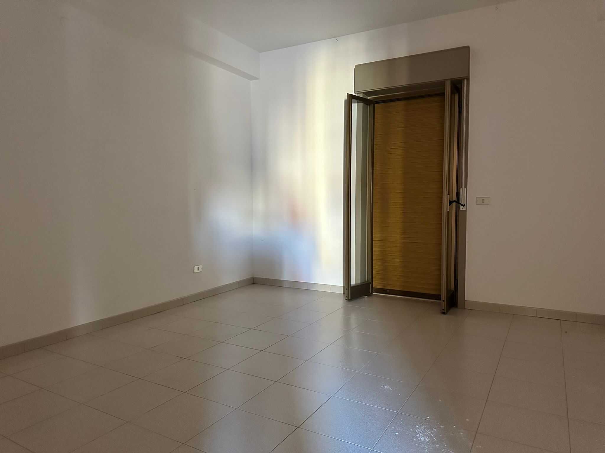 Aria vuota e luminosa con porta finestra in legno e persiana, ideale per un soggiorno o camera da letto, in un appartamento moderno in vendita o affitto a NextCasa.