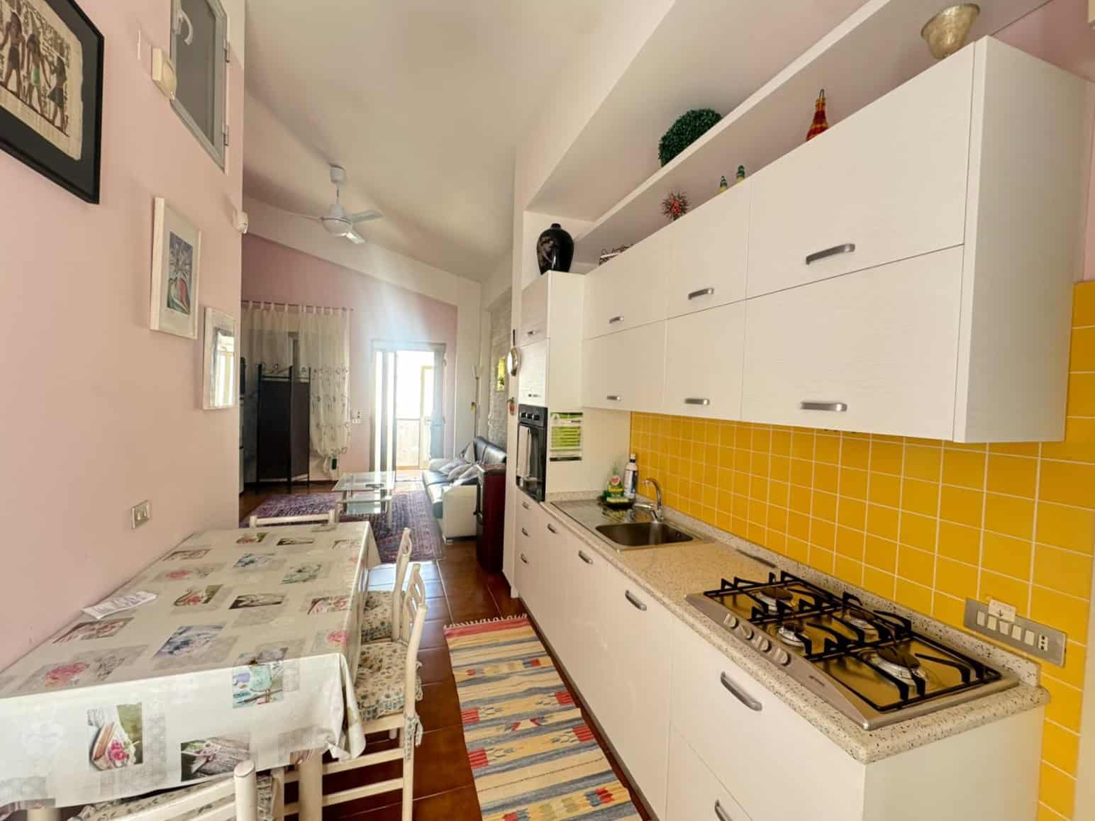 Lavagna di cucina moderna con mobili bianchi, piano cottura a gas e parete gialla, in un appartamento luminoso e accogliente, ideale per soggiorni confortevoli e funzionali.