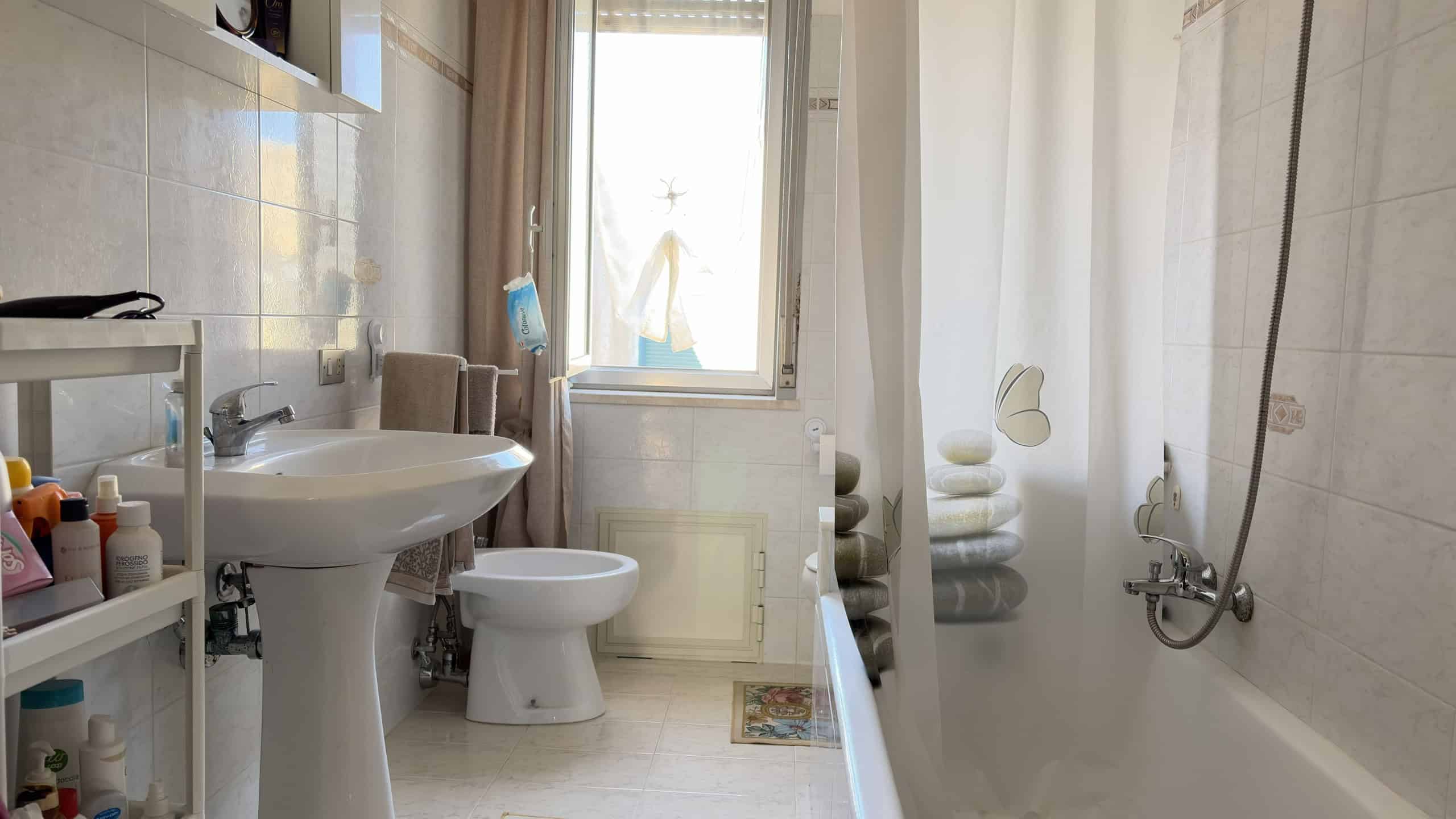 Lavabo e vasca da bagno in un bagno moderno con luce naturale, piastrelle chiare e accessori bagno essenziali, ideale per soluzioni di arredamento bagno di alta qualità.