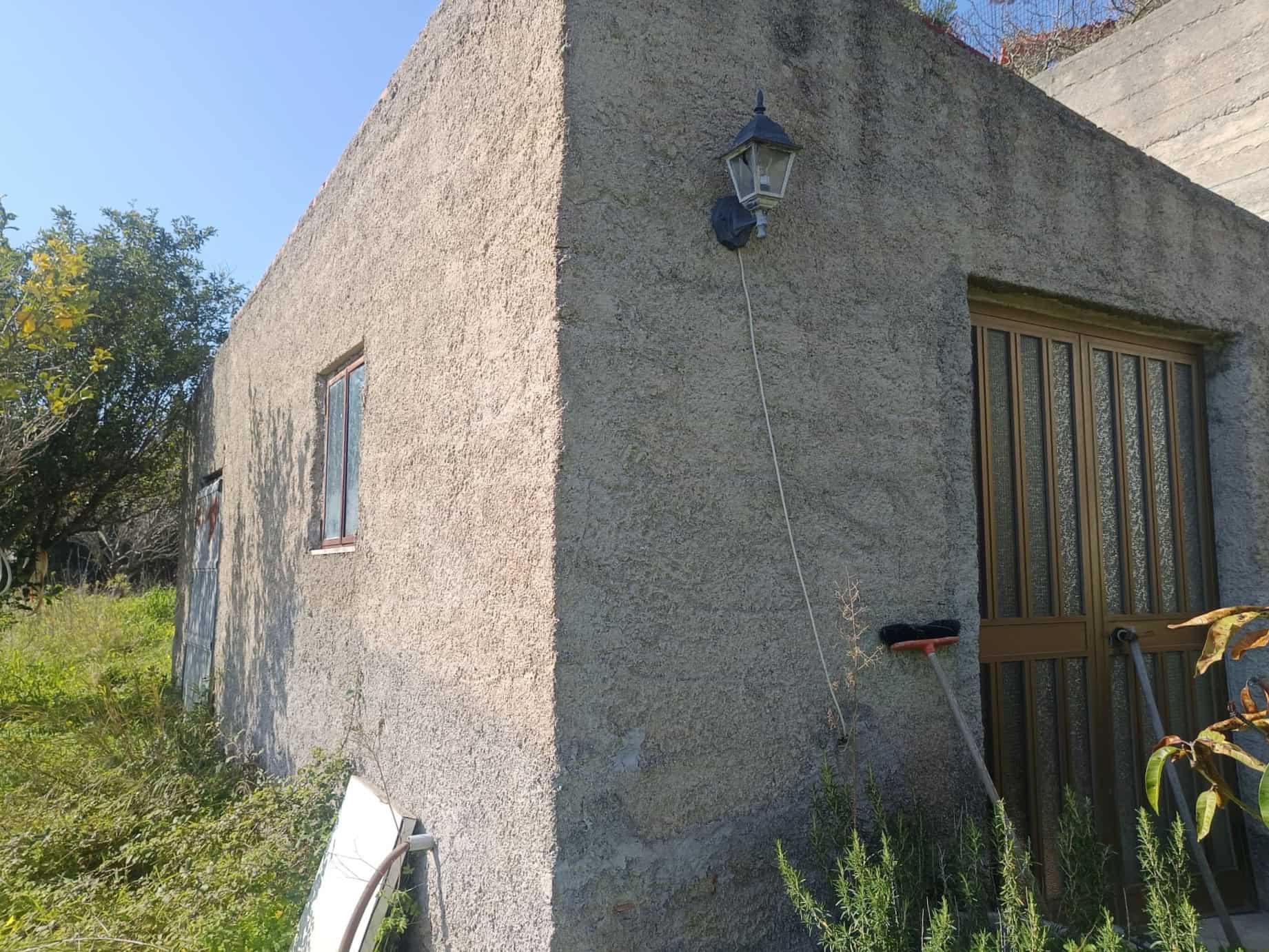 Pannello solare installato sulla parete di una casa in campagna, con lampione esterno e giardino verde circostante.