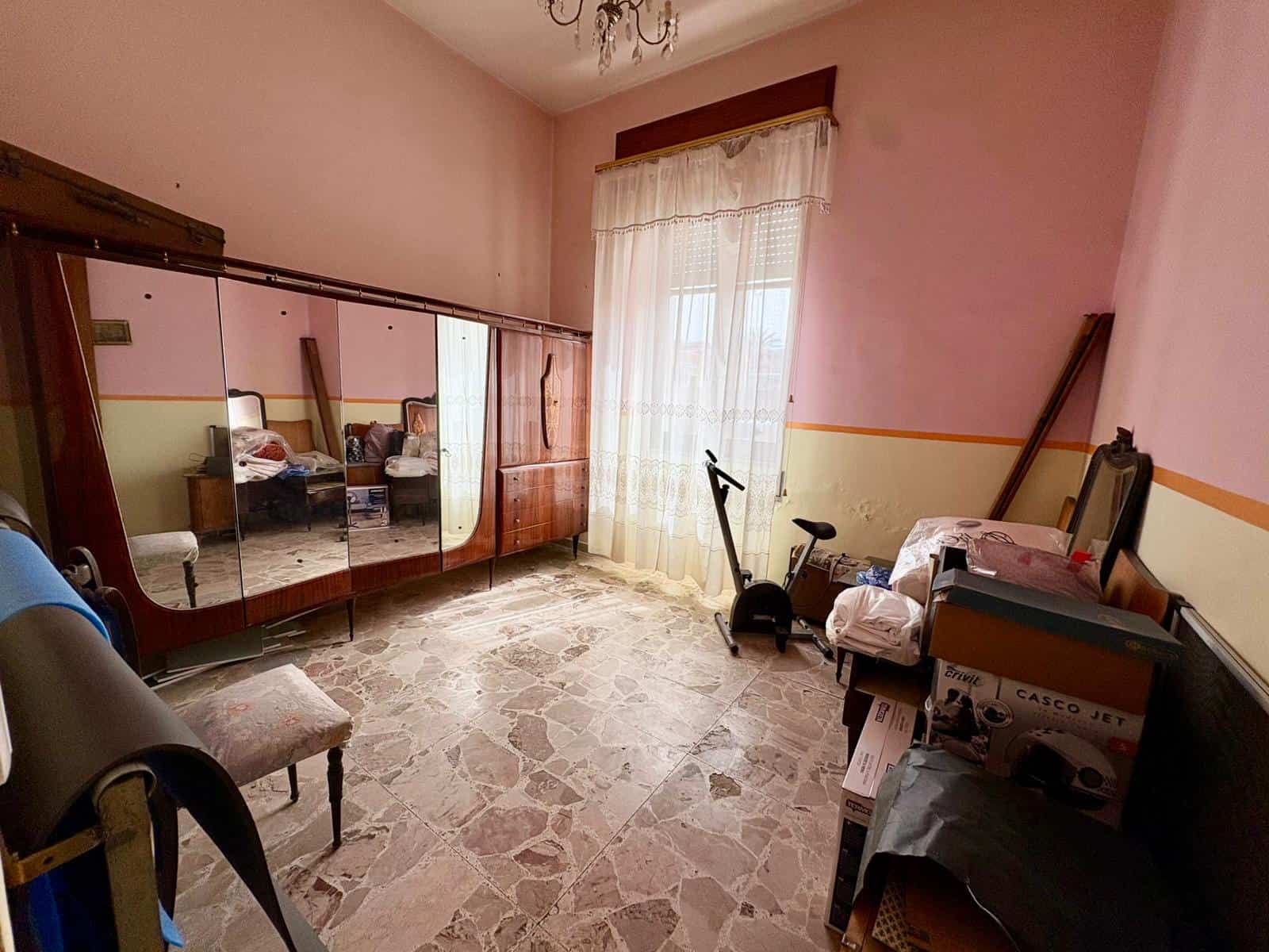 Camera da letto con armadio a specchio, sedia, e attrezzature per esercizi, illuminata da luce naturale, con pareti rosa e pavimento in marmo.