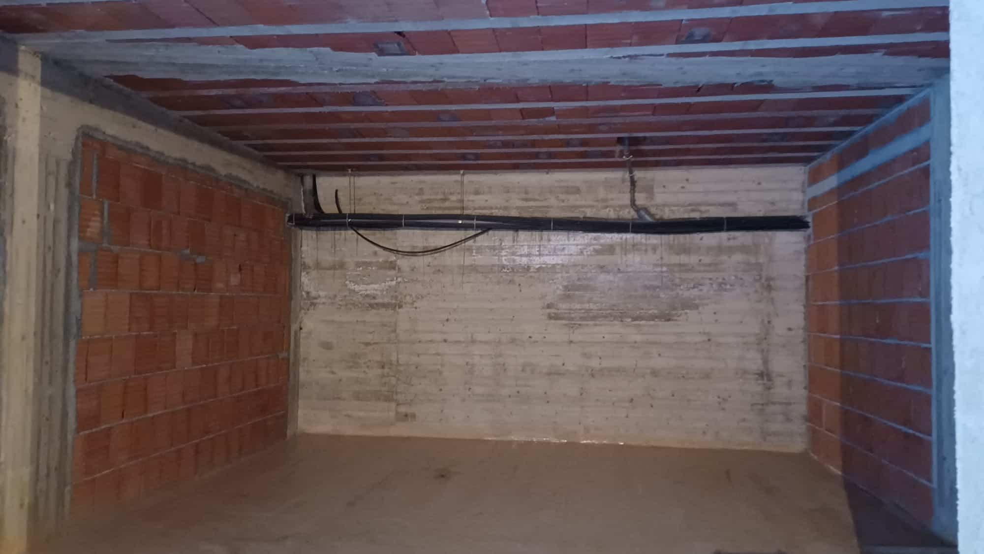 Pannello di pareti in cemento e mattoni in un ambiente di costruzione o ristrutturazione, con tubature visibili sul soffitto.