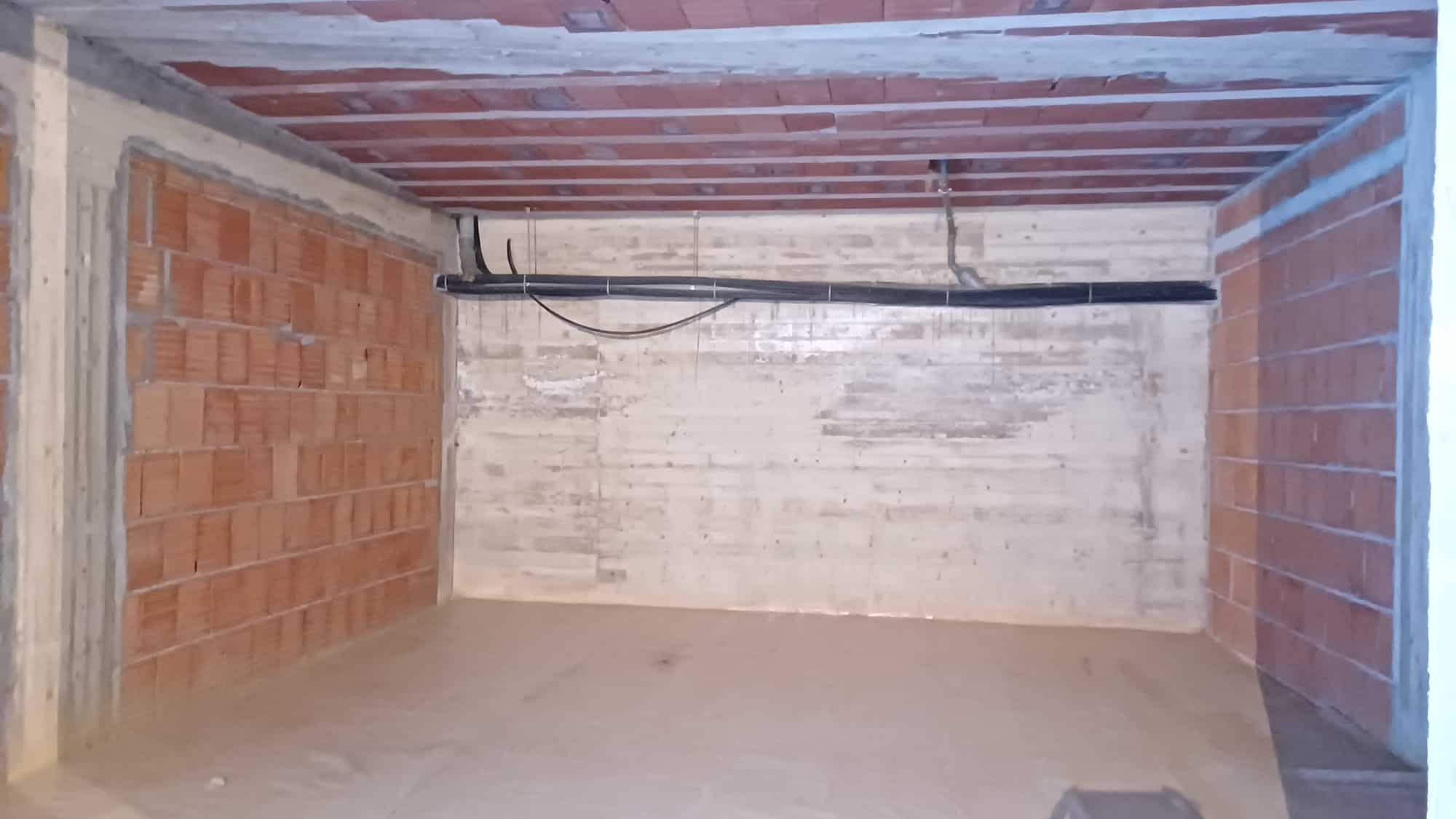 Serranda di un garage o magazzino in costruzione con pareti in mattoni e soffitto in legno, pronto per essere rifinito e arredato.