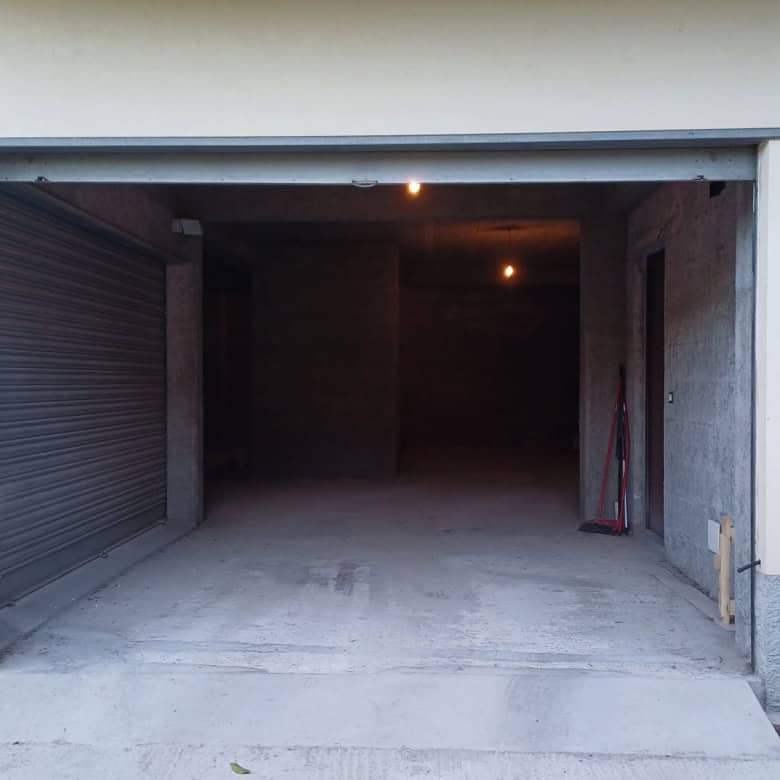 Automobile garage con apertura a basculante in edificio residenziale, spazio per auto e deposito, con pareti in cemento e pavimento in calcestruzzo.