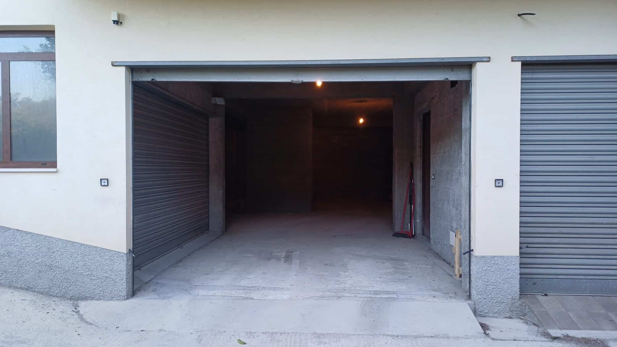Automobile garage con apertura a basculante in edificio residenziale, spazio per auto e deposito, con pareti in cemento e pavimento in calcestruzzo.