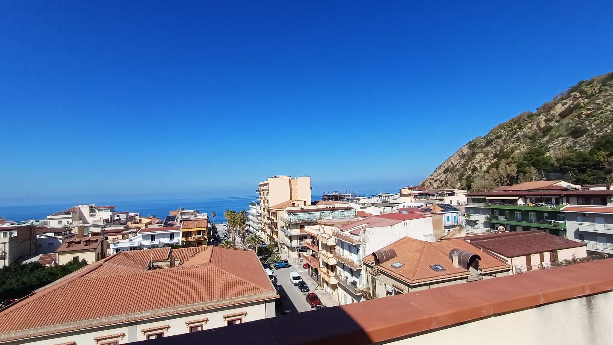 Vista panoramica delle case di NextCasa con il mare sullo sfondo, montagna a destra e cielo sereno, rappresentando un quartiere residenziale in una località costiera italiana.