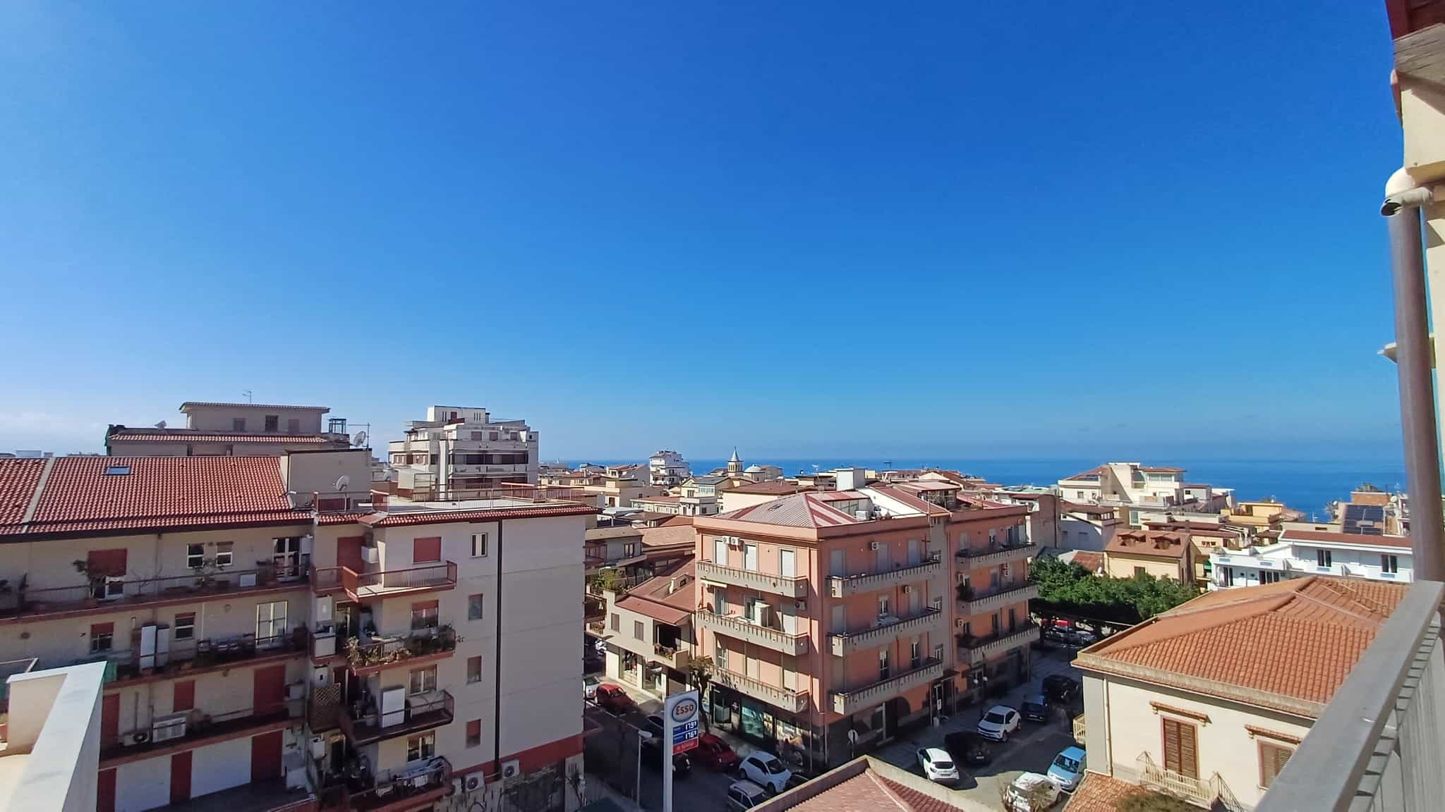 Ampia vista panoramica sulla città e sul mare dal balcone di un appartamento in zona residenziale, con edifici moderni e cielo sereno.