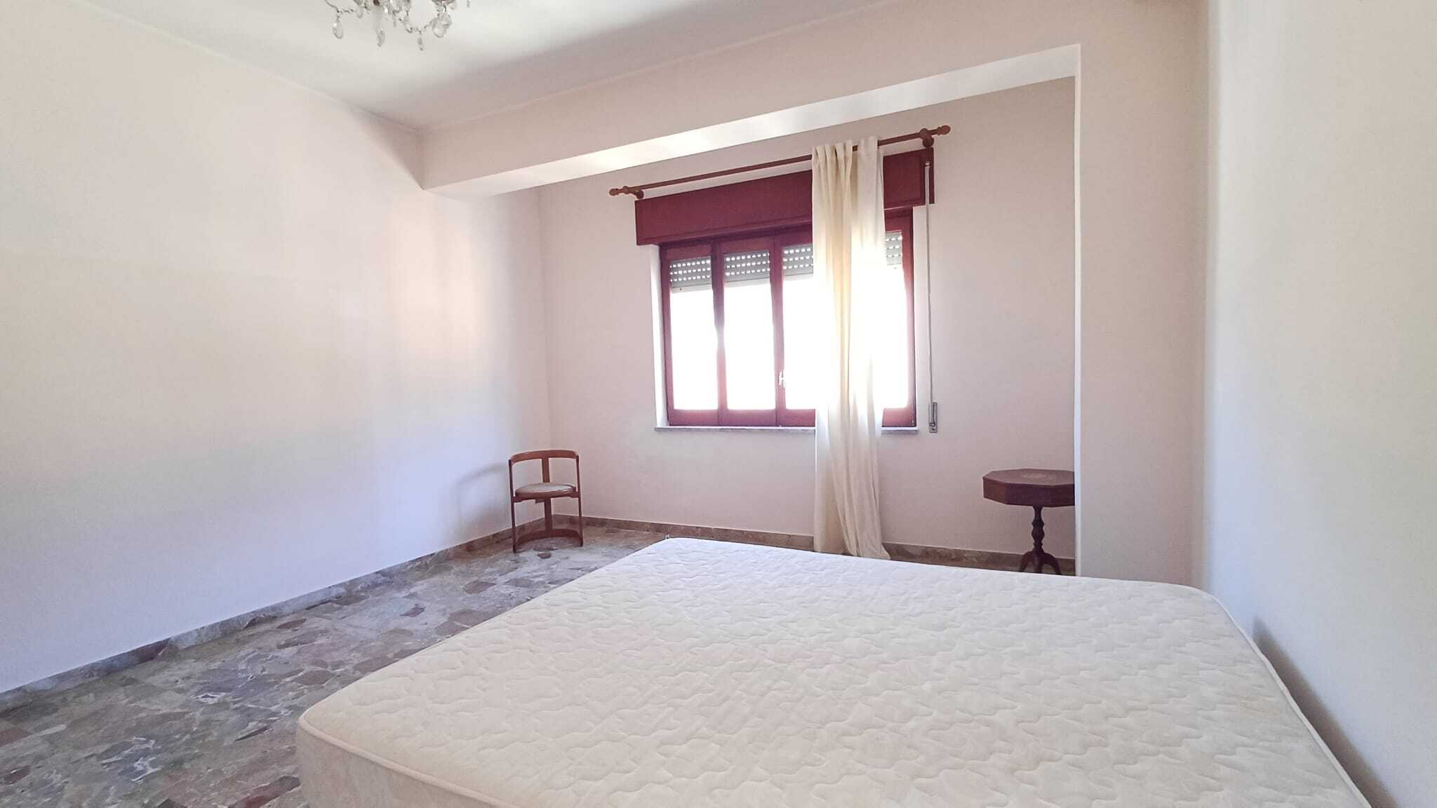 Ampia camera da letto vuota con finestra, tende bianche e mobili minimalisti, ideale per affitto o vendita immobiliare.