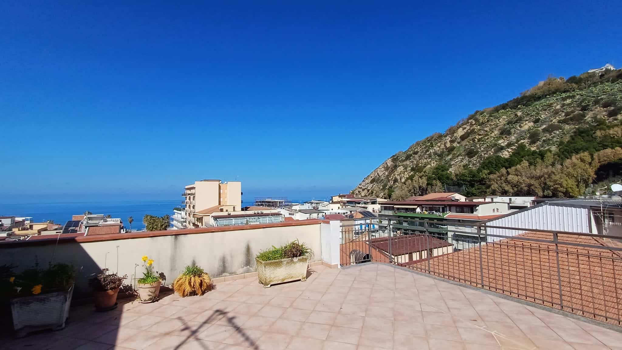 Aggiunta di un ampio terrazzo con vista mare e montagna, con piante in vaso e pavimentazione in piastrelle, ideale per relax e convivialità all'aperto.