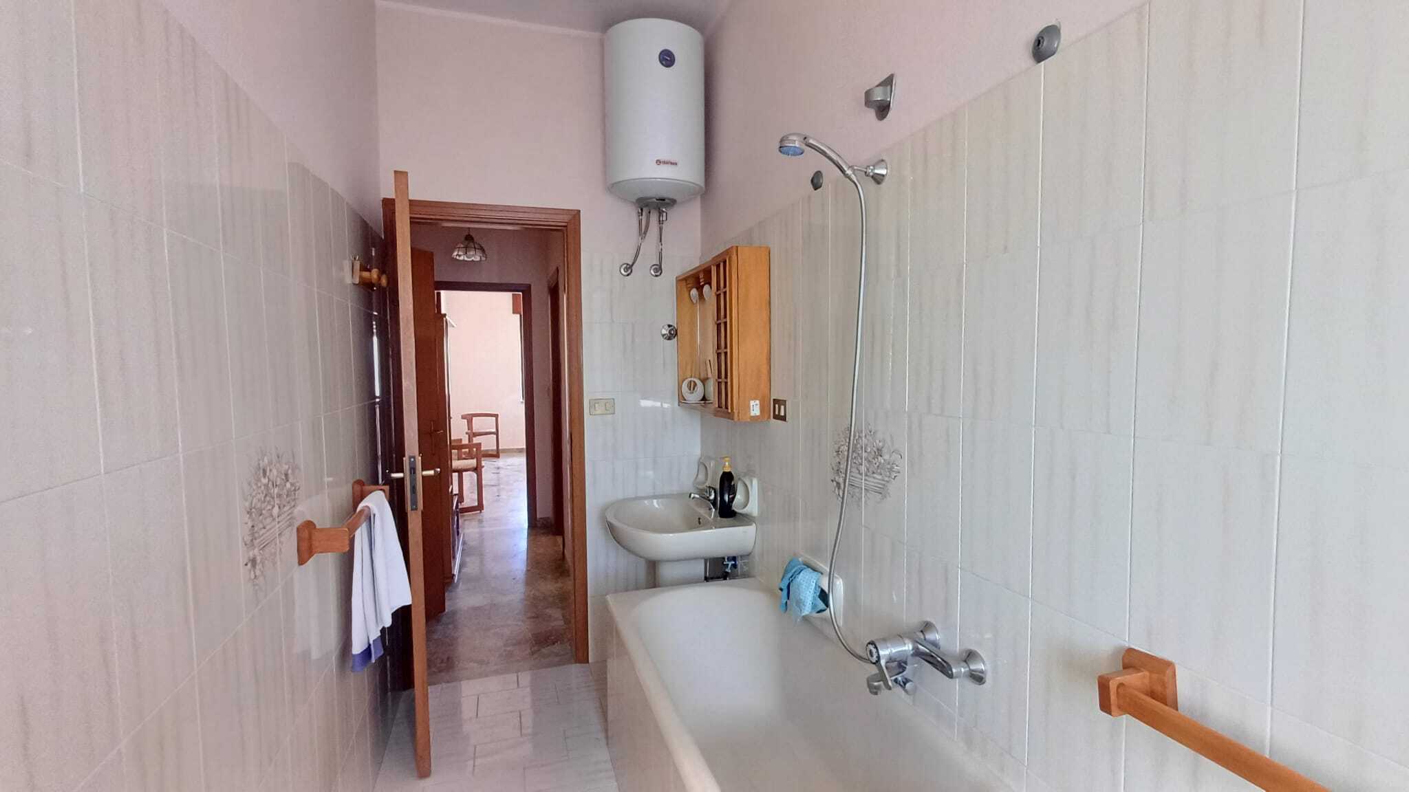 Acqua calda e doccia in bagno con pareti rivestite di piastrelle chiare, accessori in legno e lavabo con specchio, ideale per ambienti di case o appartamenti in vendita o affitto.