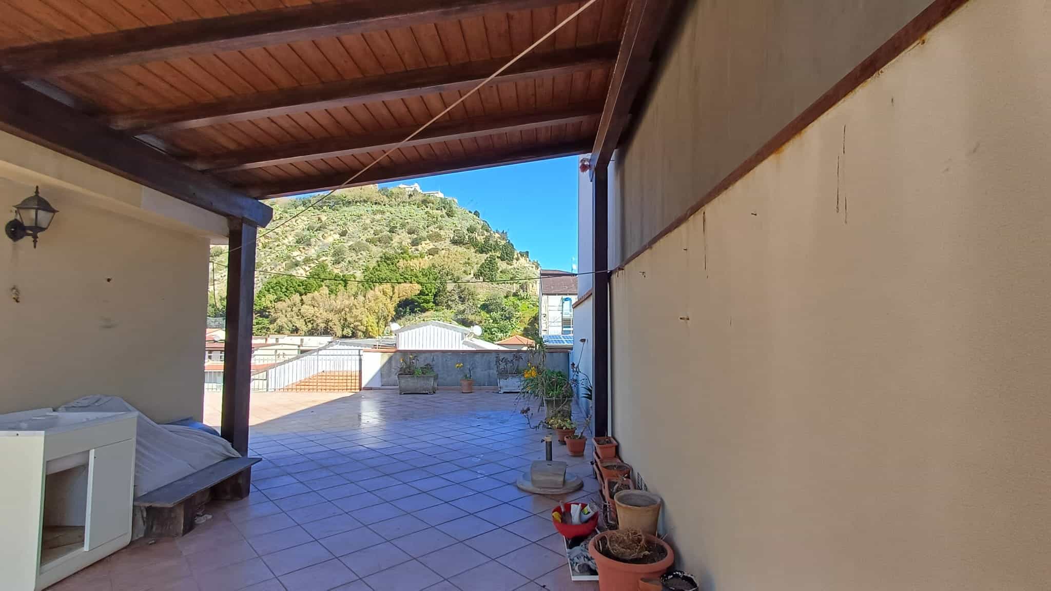 Balcone con vista panoramica su colline verdi e cielo azzurro, spazio esterno con piastrelle e piante in vaso, ideale per relax e momenti all'aperto.