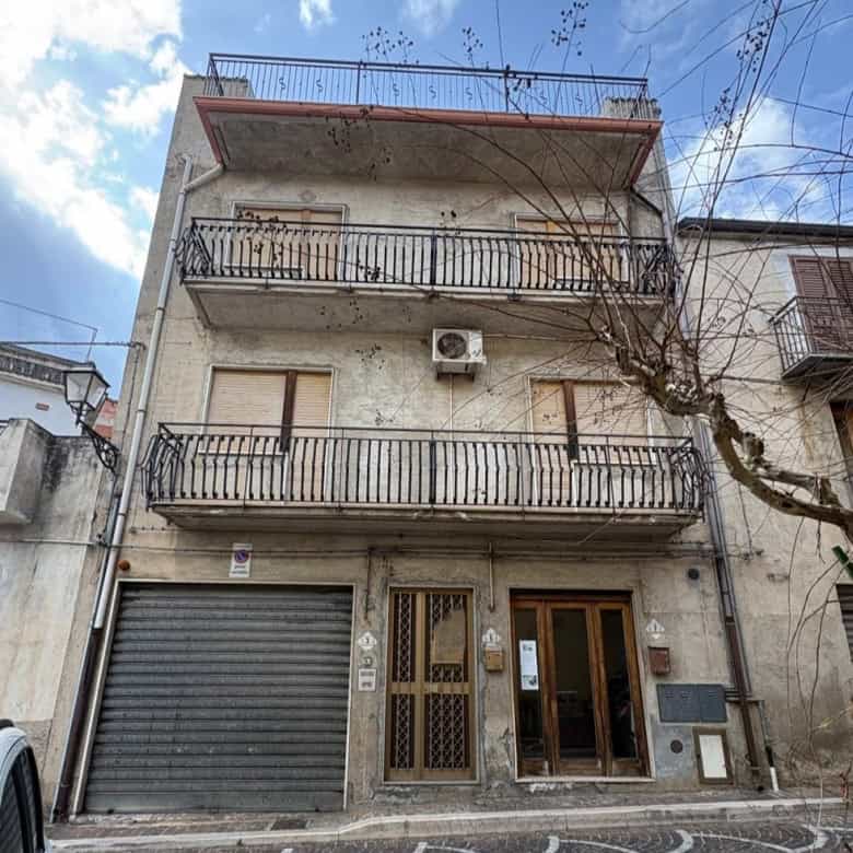 Ampio edificio residenziale con balconi in ferro battuto, facciata in pietra e garage, situato in zona urbana di Napoli, Italia, con cielo sereno e alberi circostanti.