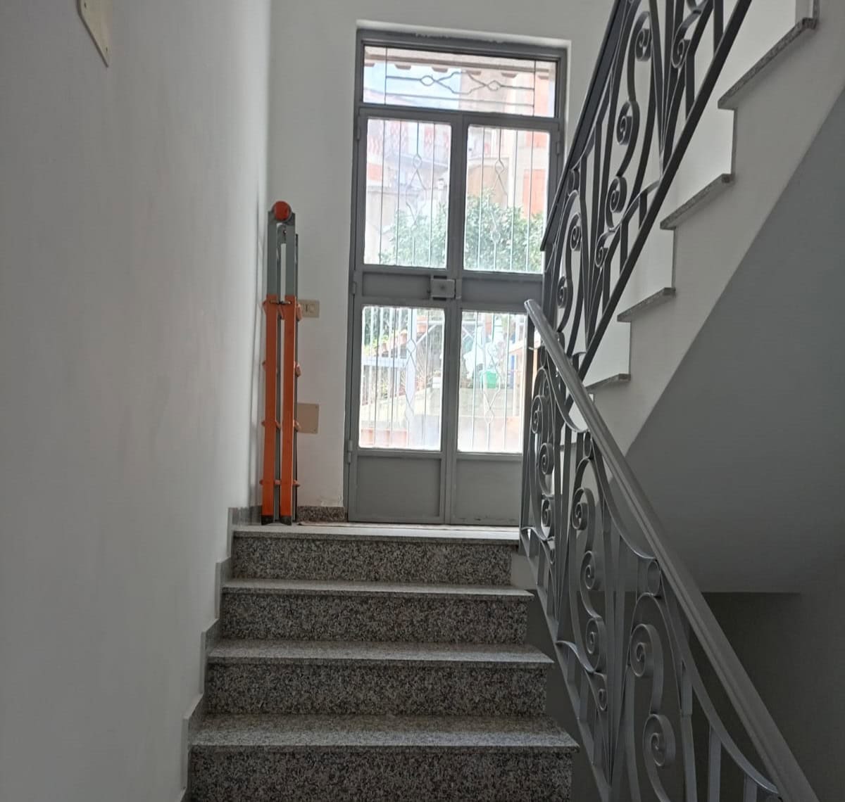 Scalinata interna con ringhiera decorativa e porta finestra in vetro, ambiente luminoso e moderno, ideale per immobili residenziali o commerciali in Italia.