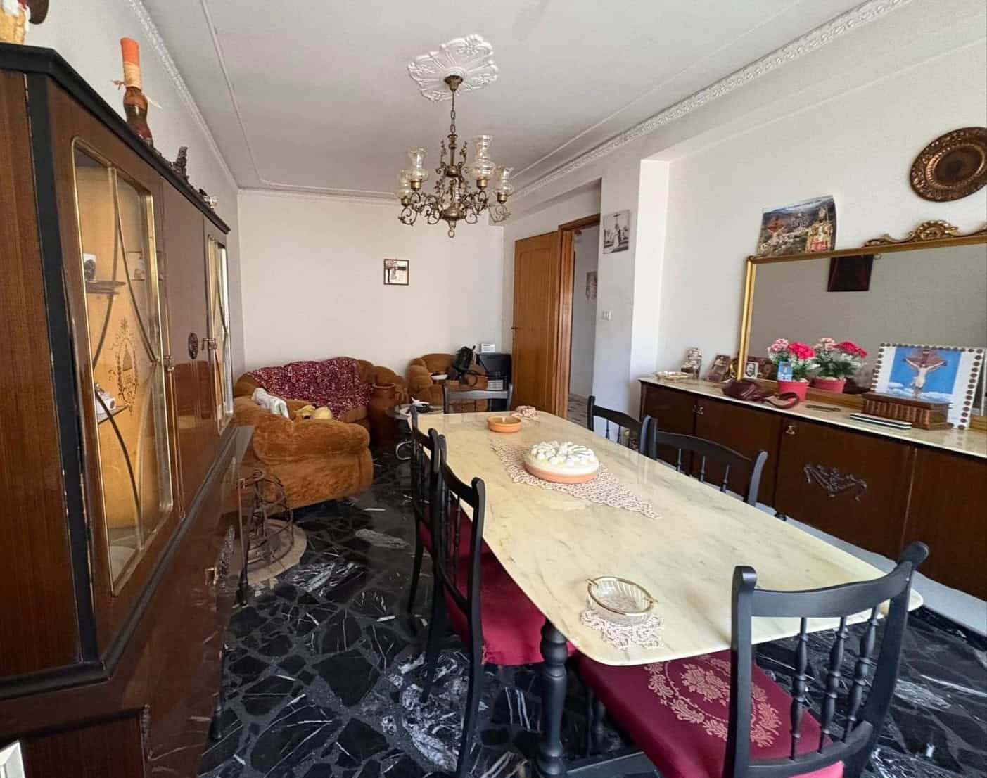 Ampia sala da pranzo con tavolo in legno, sedie imbottite rosse, arredi vintage, e decorazioni tradizionali, illuminata da lampadario elegante, ideale per convivialità e incontri familiari.