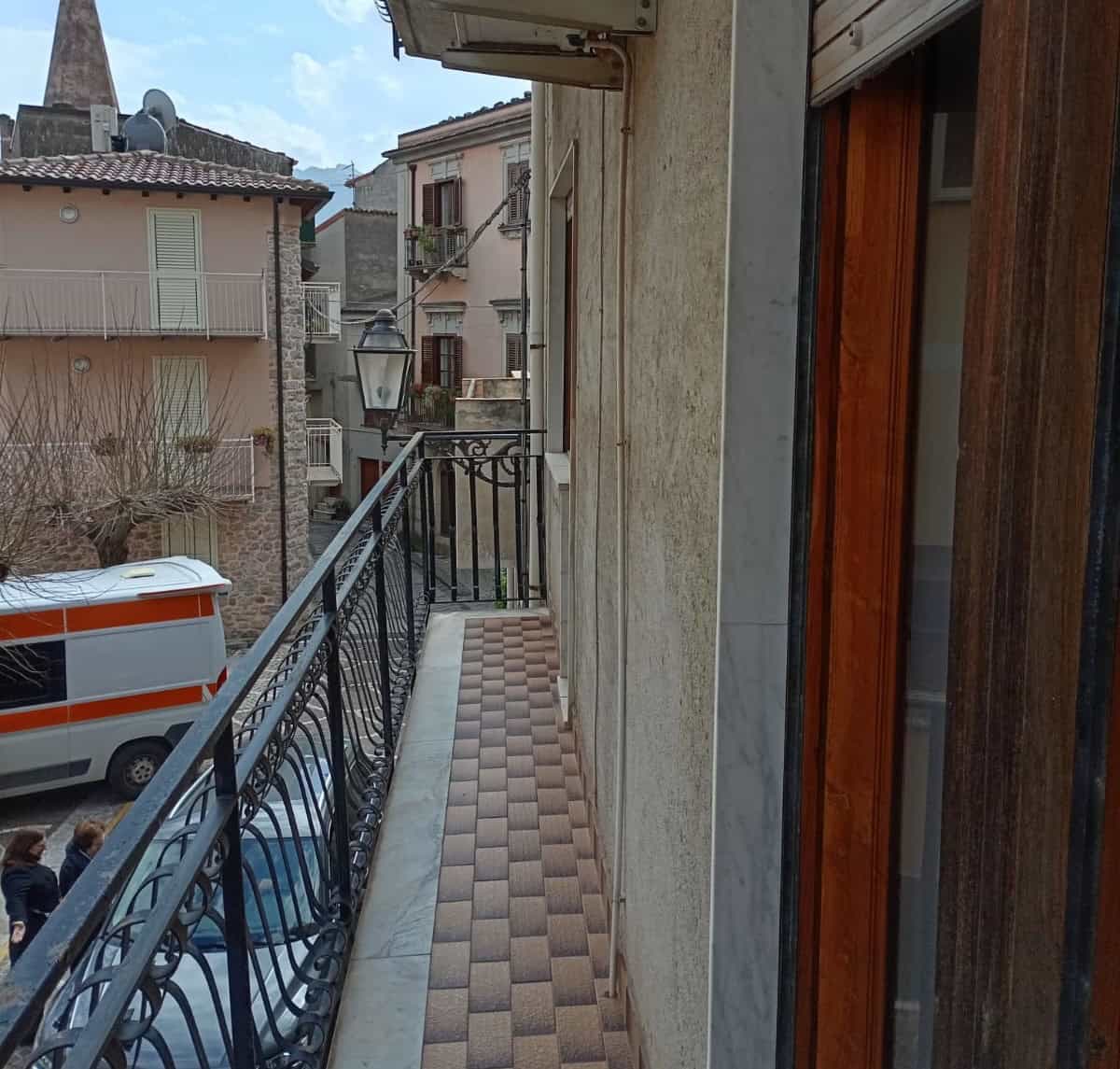 Balcone di un appartamento con ringhiera in ferro battuto, pavimentazione in piastrelle colorate, vista su strada e edifici storici in un quartiere residenziale.