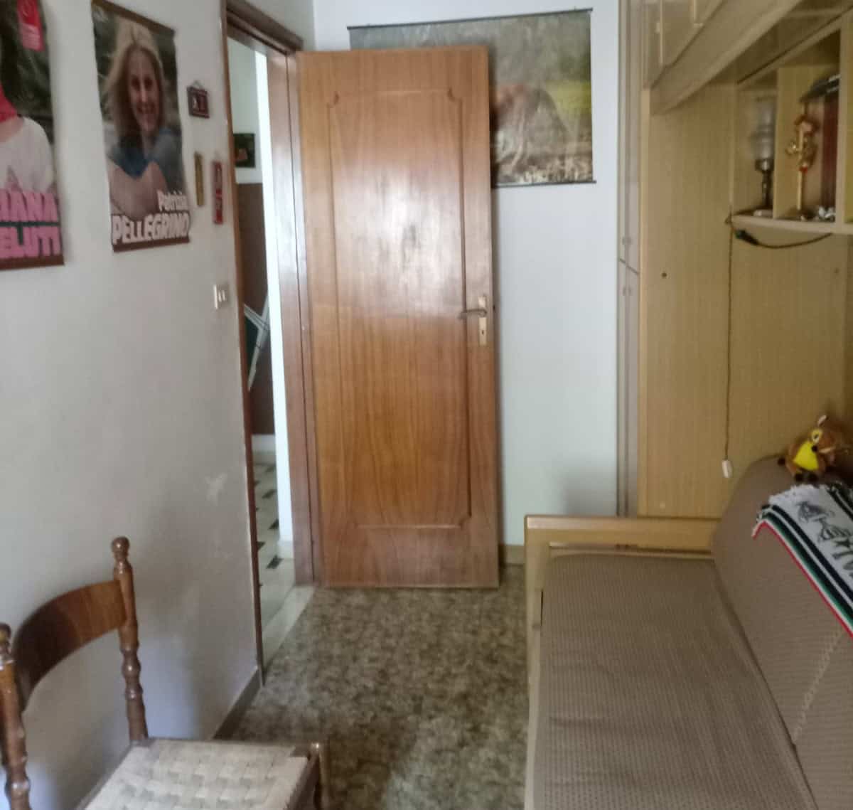Porta in legno in una stanza con arredi semplici, pareti decorate con poster e quadri, ambiente domestico accogliente e informale.