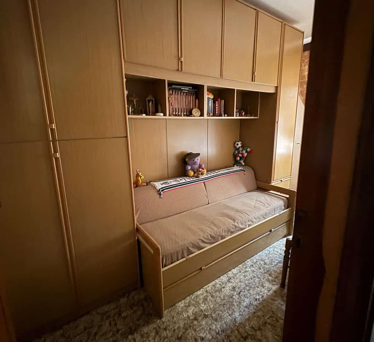 Letto a scomparsa con armadio a muro in legno chiaro, stanza da letto accogliente con scaffali e decorazioni, ideale per ambienti di case o appartamenti.