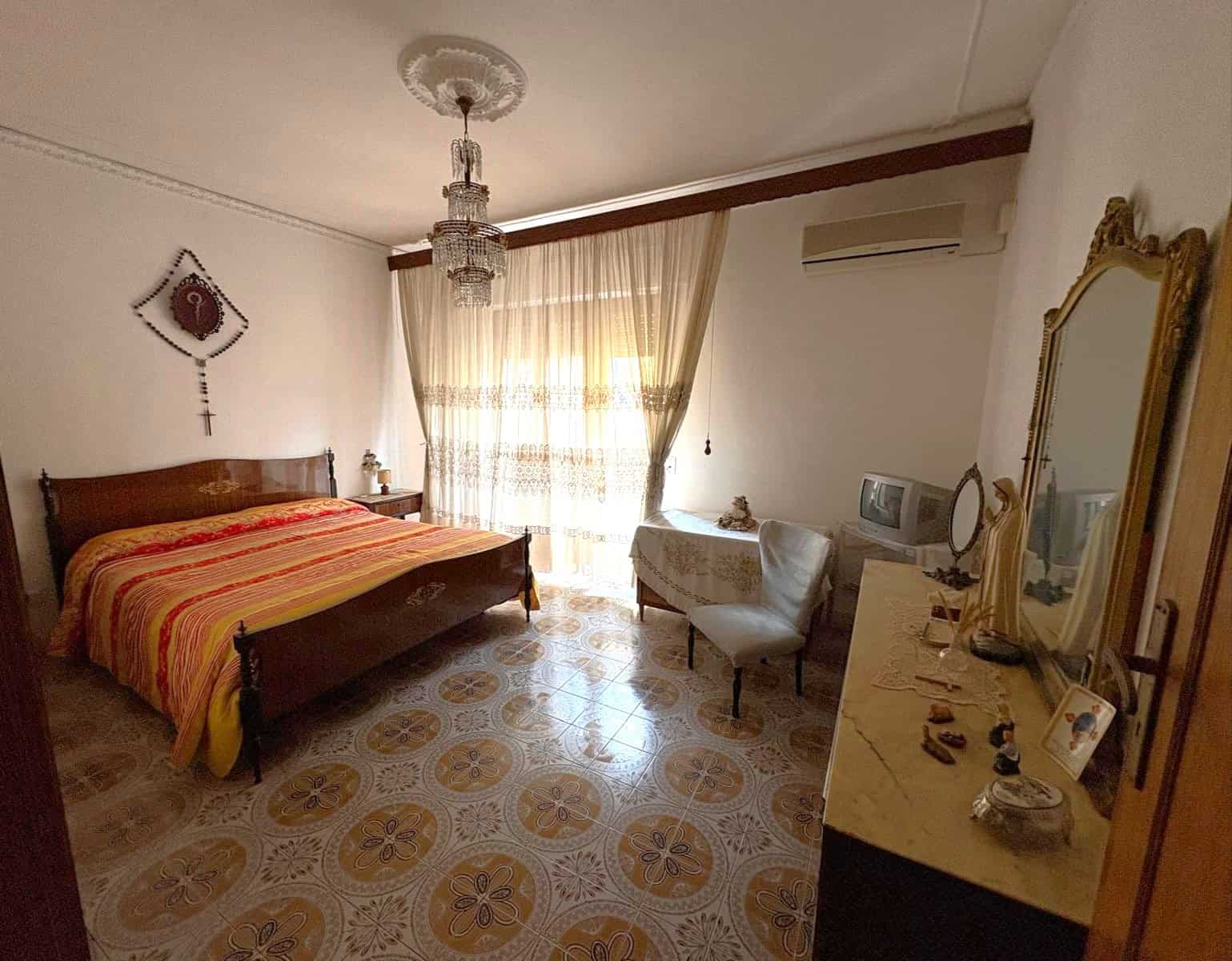 Letto matrimoniale in camera da letto con arredi eleganti e decorazioni classiche, luce naturale che entra dalle tende, ambiente accogliente e spazioso.