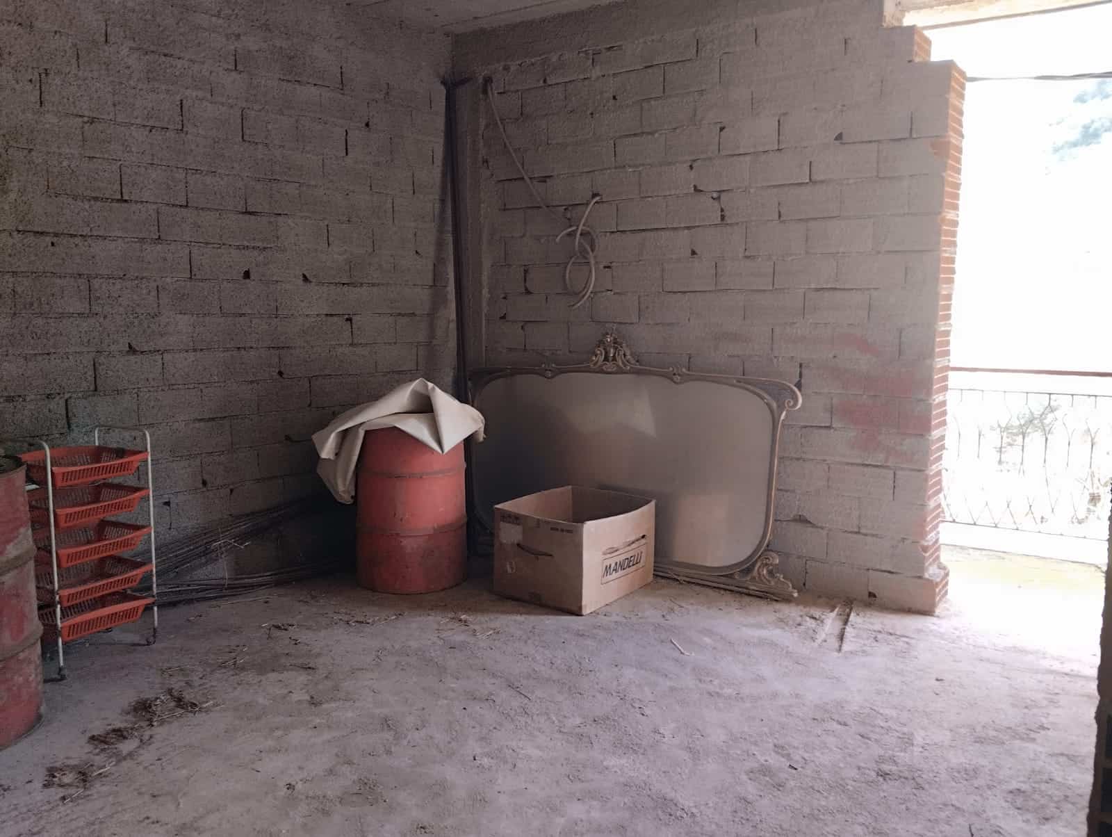 Il testo dell'immagine mostra un ambiente in fase di ristrutturazione con pareti in mattoni a vista, un radiatore da installare e alcuni materiali di costruzione come tubi e scatole.