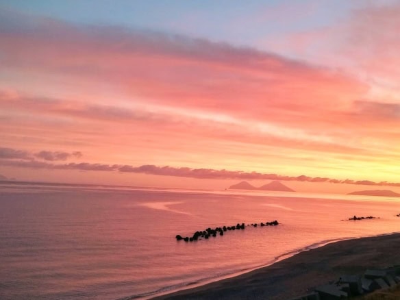 Tramonto sul mare con cielo rosa e arancione, spiaggia tranquilla e onde calme, perfetta per relax e passeggiate serali in un ambiente naturale e suggestivo.