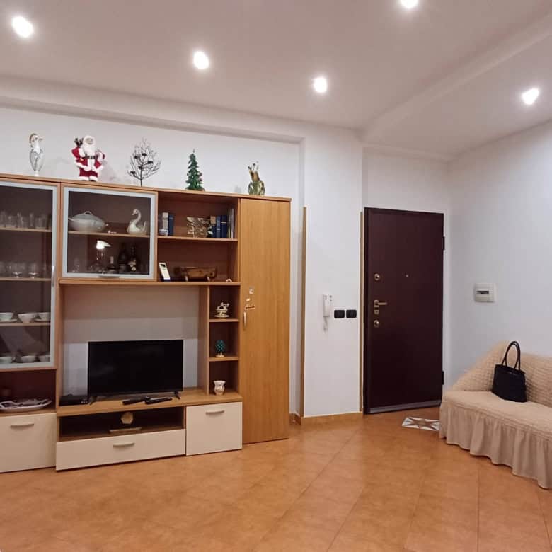 Elegante soggiorno con mobile porta TV, divano beige e decorazioni natalizie, ideale per vivere momenti di relax e convivialità in un ambiente accogliente e ben illuminato.