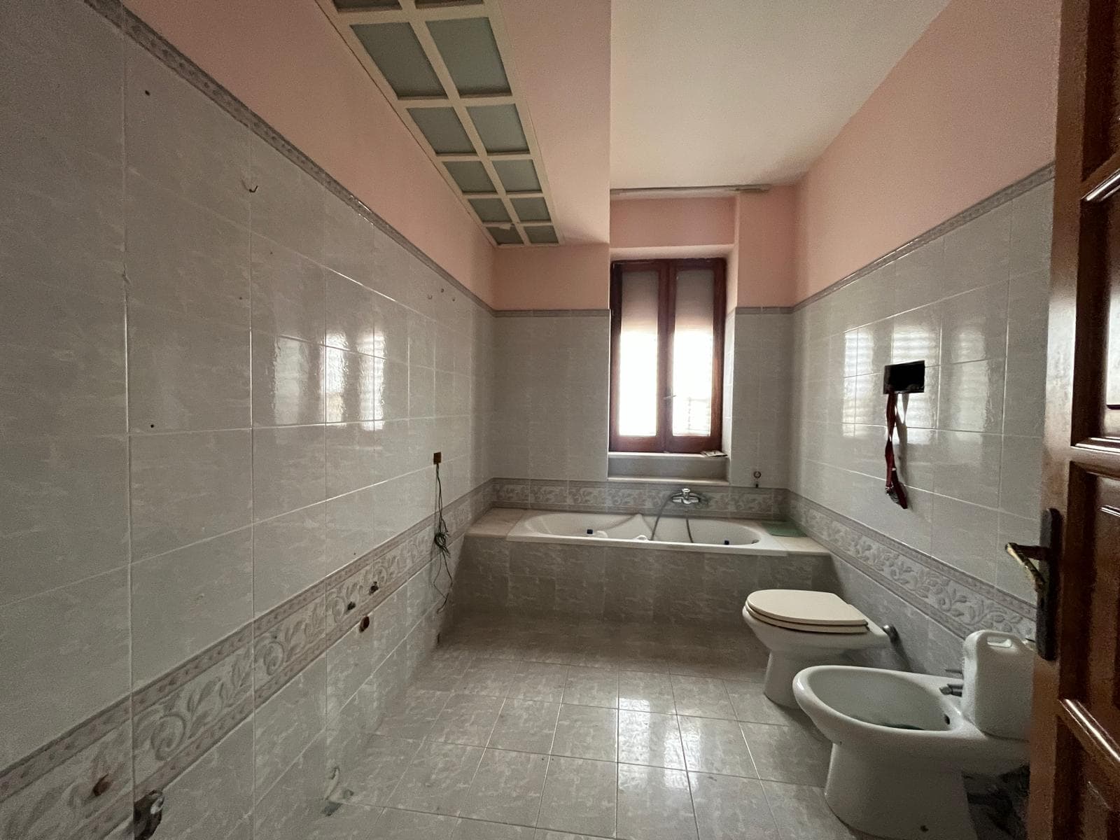 Acqua calda e vasca da bagno in un bagno spazioso e luminoso con pareti rivestite di piastrelle chiare e finestra grande per ventilazione naturale.
