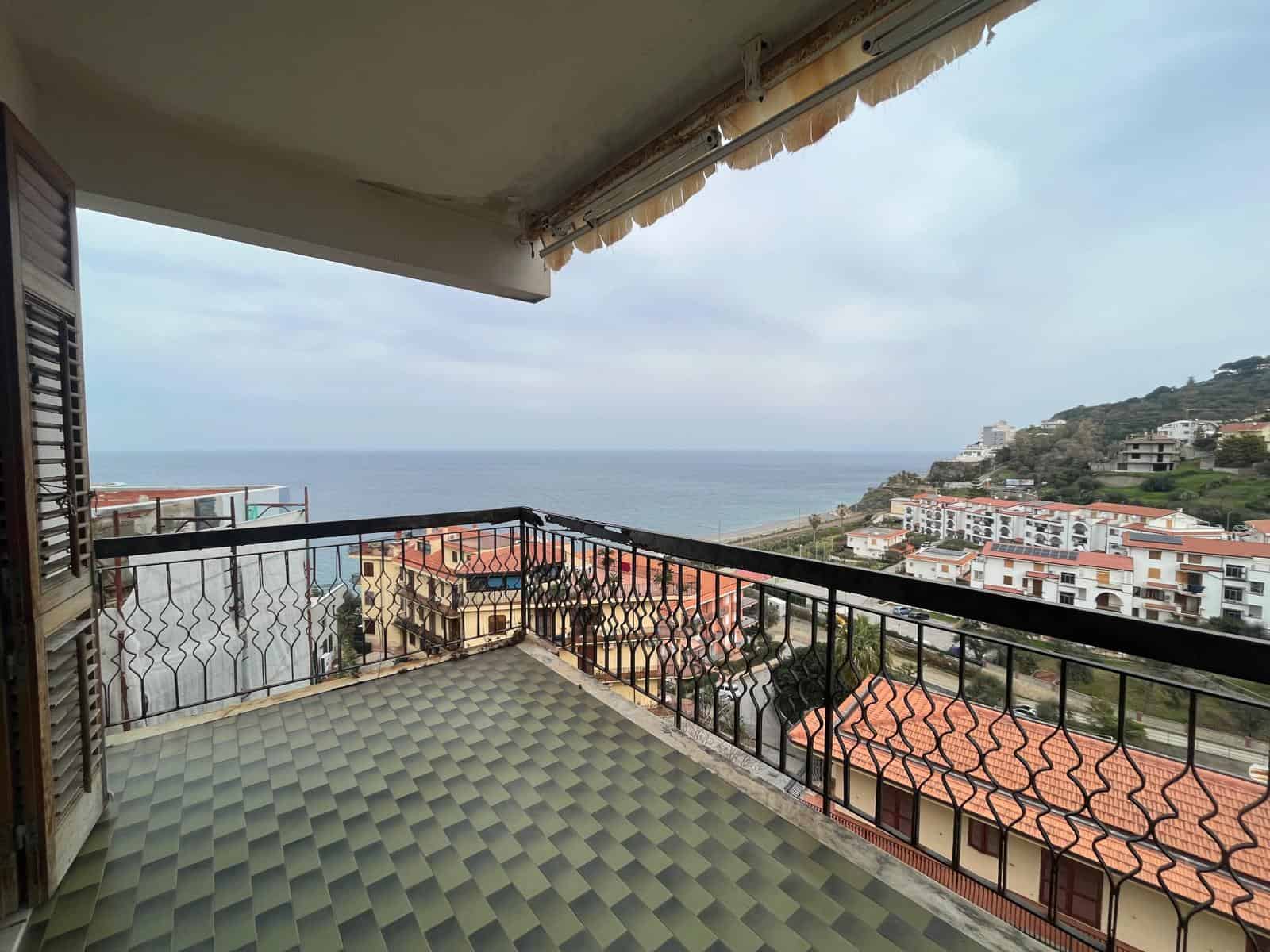 Balcone con vista mare, arredato con pavimento in piastrelle verdi e ringhiera in ferro, offre un panorama panoramico sulla costa e le case circostanti, ideale per relax e momenti all'aperto.
