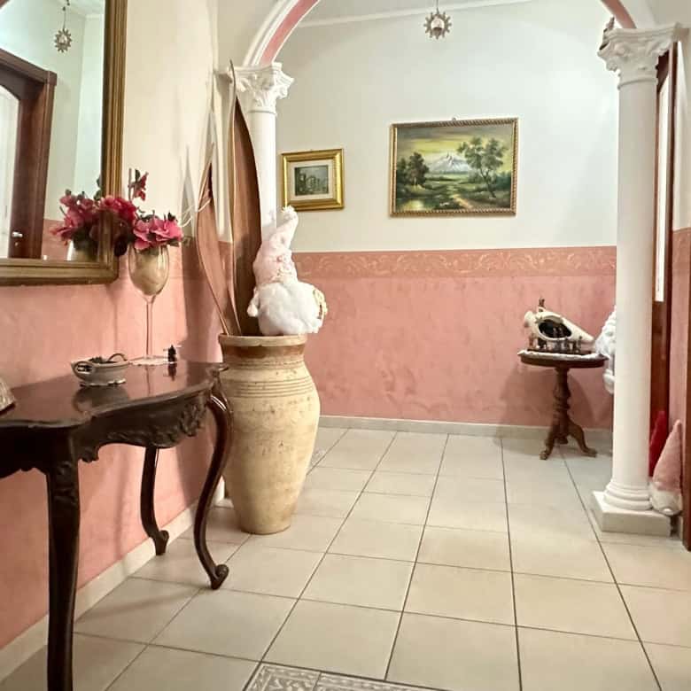Elegante ingresso con pareti rosa, decorato con fiori e opere d'arte, arricchito da colonne bianche e mobili classici, creando un'atmosfera accogliente e raffinata.