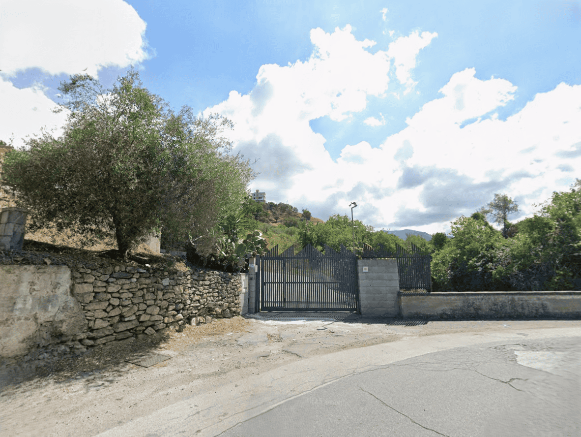 Cancello in ferro battuto con muro in pietra, ingresso a proprietà privata immersa nel verde, paesaggio rurale in Toscana, Italia.