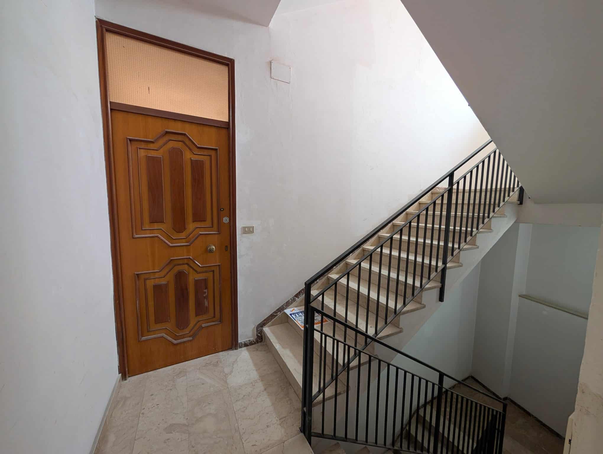 Porte in legno all'ingresso di un appartamento con scala in metallo, ambiente luminoso e pulito, ideale per immagini di immobili residenziali e interni di case in vendita o affitto.