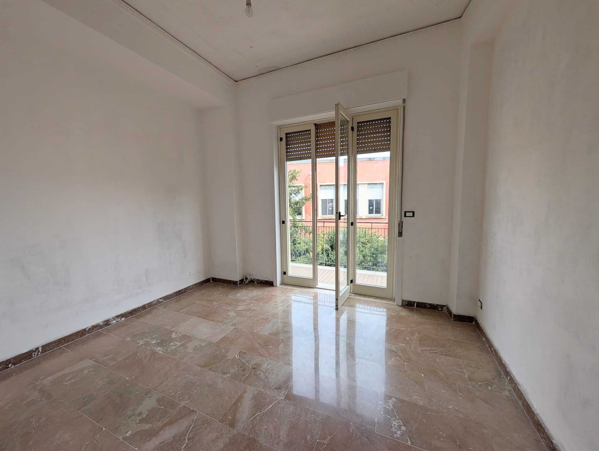 Stanza vuota in fase di ristrutturazione con porta finestra e vista sul giardino, ideale per soggiorno o camera da letto.