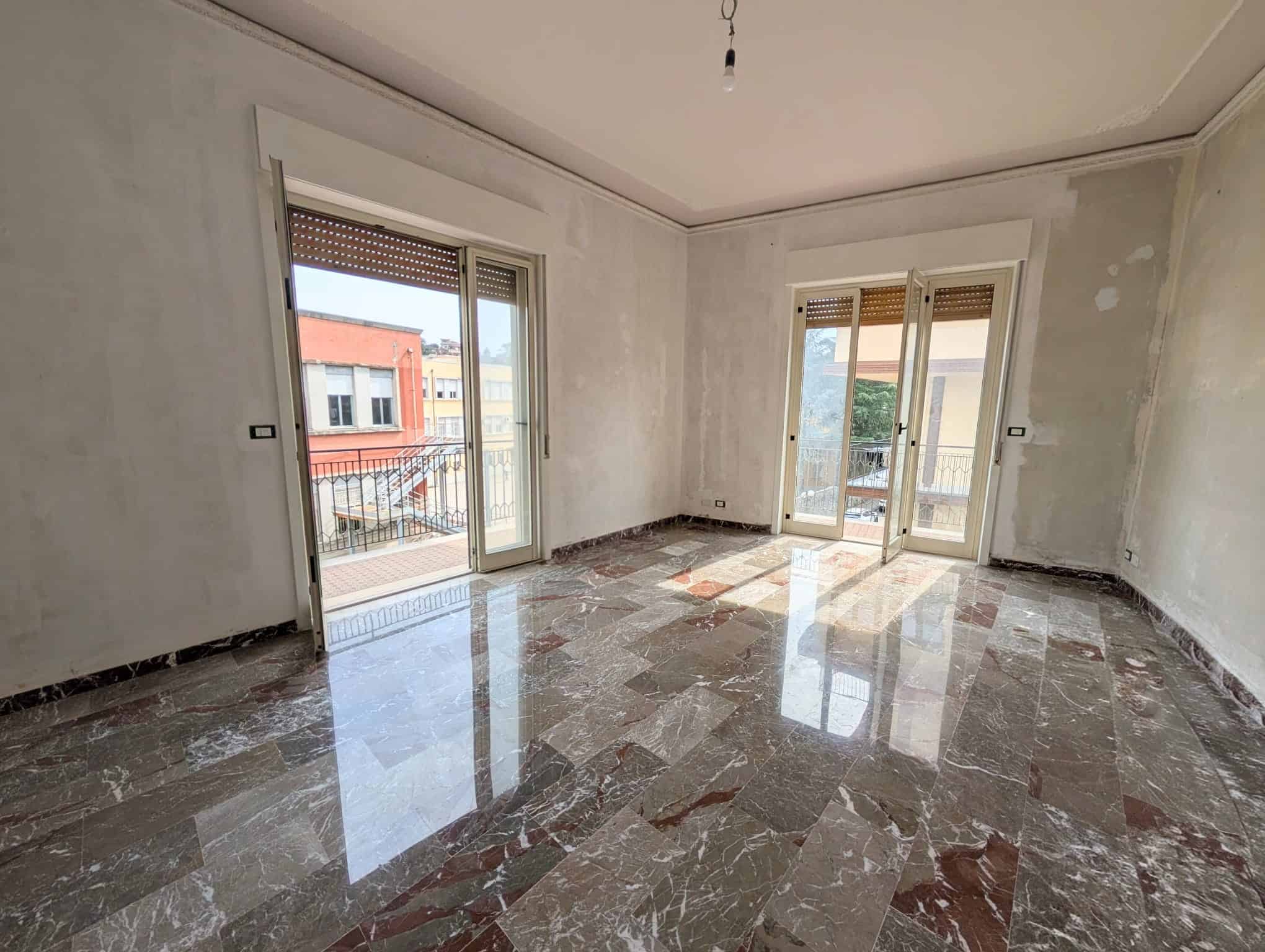 Interno di un appartamento in fase di ristrutturazione con grandi finestre e pavimento in marmo lucido, pronto per essere arredato.