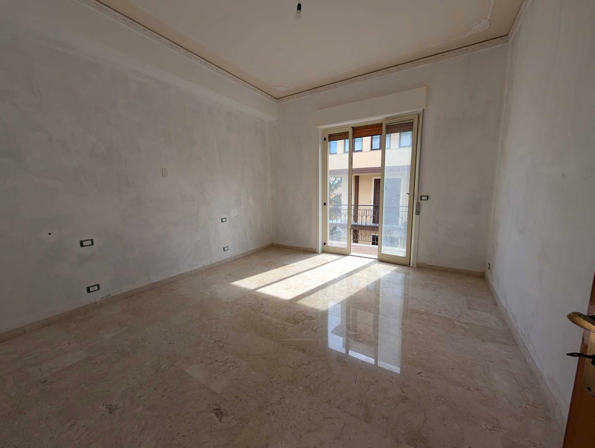 Appartamento in fase di ristrutturazione con pareti bianche e grande finestra con balcone, luminoso e spazioso, ideale per soggiorno o camera da letto, pronto per personalizzazione.