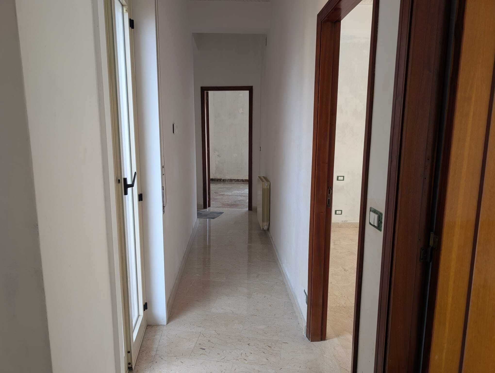 Corridoio interno di un appartamento in fase di ristrutturazione, con pareti bianche e pavimento in marmo chiaro, pronto per essere arredato.