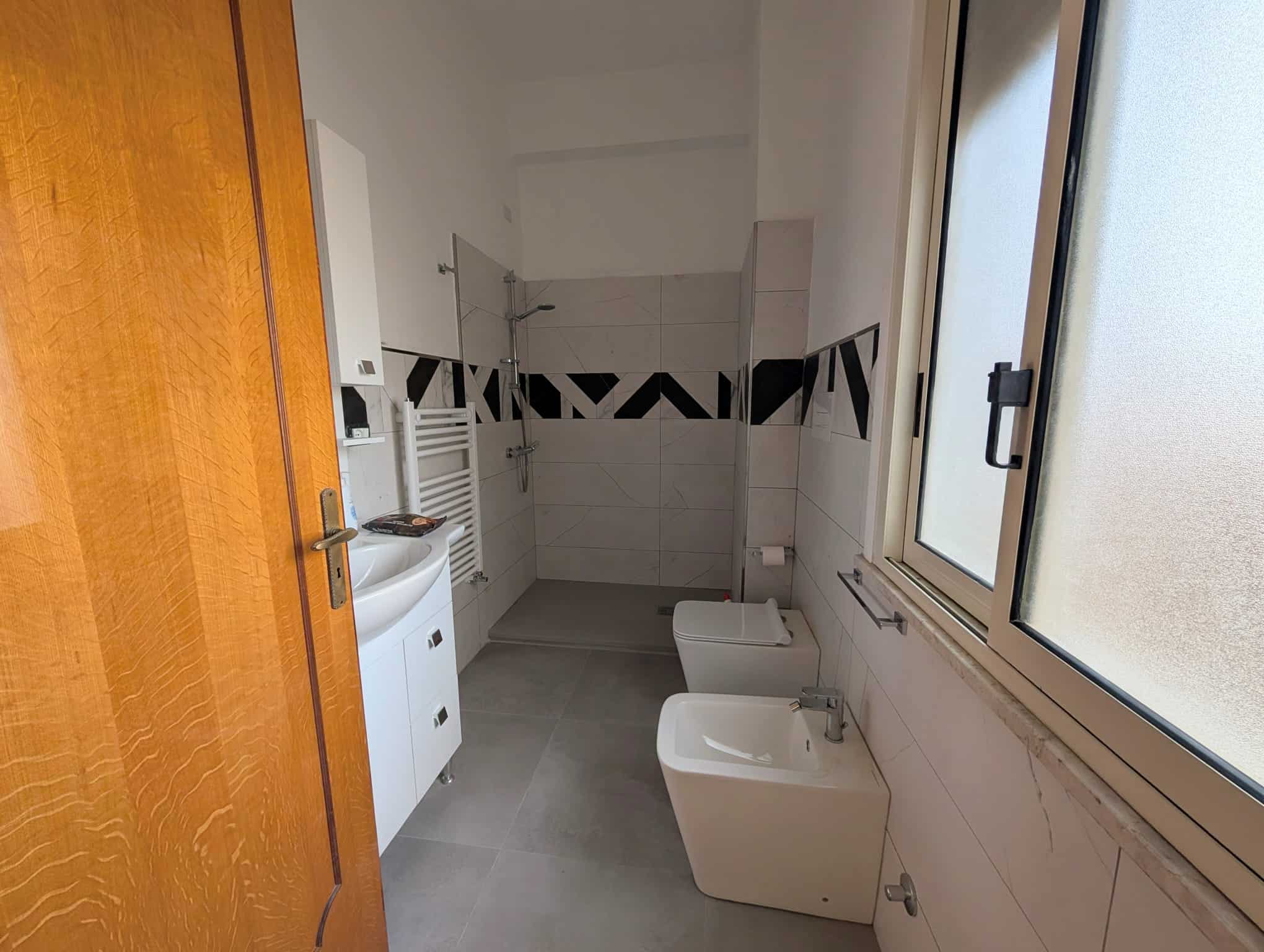 Lavanderia moderna con lavabo, bidet e finestra grande, ambiente luminoso e funzionale per la cura della casa.