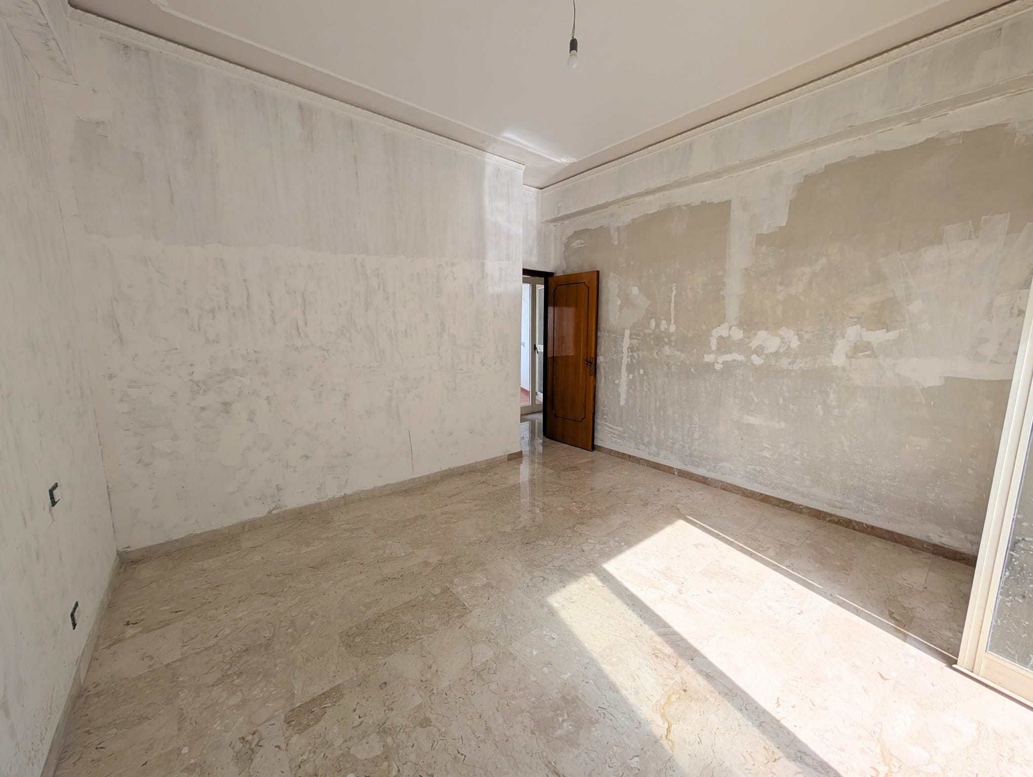 Stanza vuota in fase di ristrutturazione con pareti in fase di preparazione e pavimento in marmo, pronta per essere personalizzata e arredata.