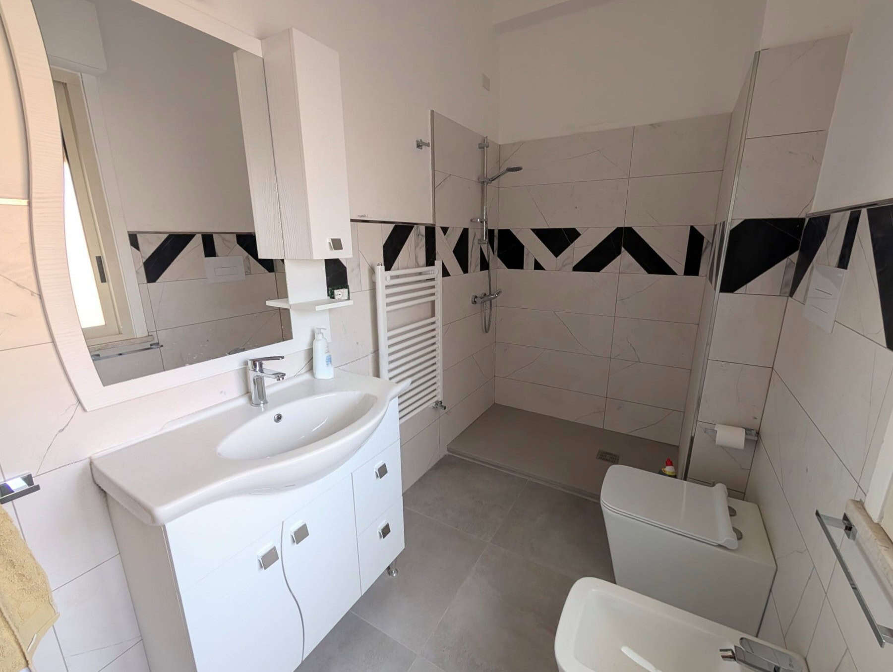 Lavabo e bagno moderno con doccia walk-in, piastrelle bianche e dettagli neri, arredi minimalisti, ideale per ristrutturazioni di case di alta qualità.
