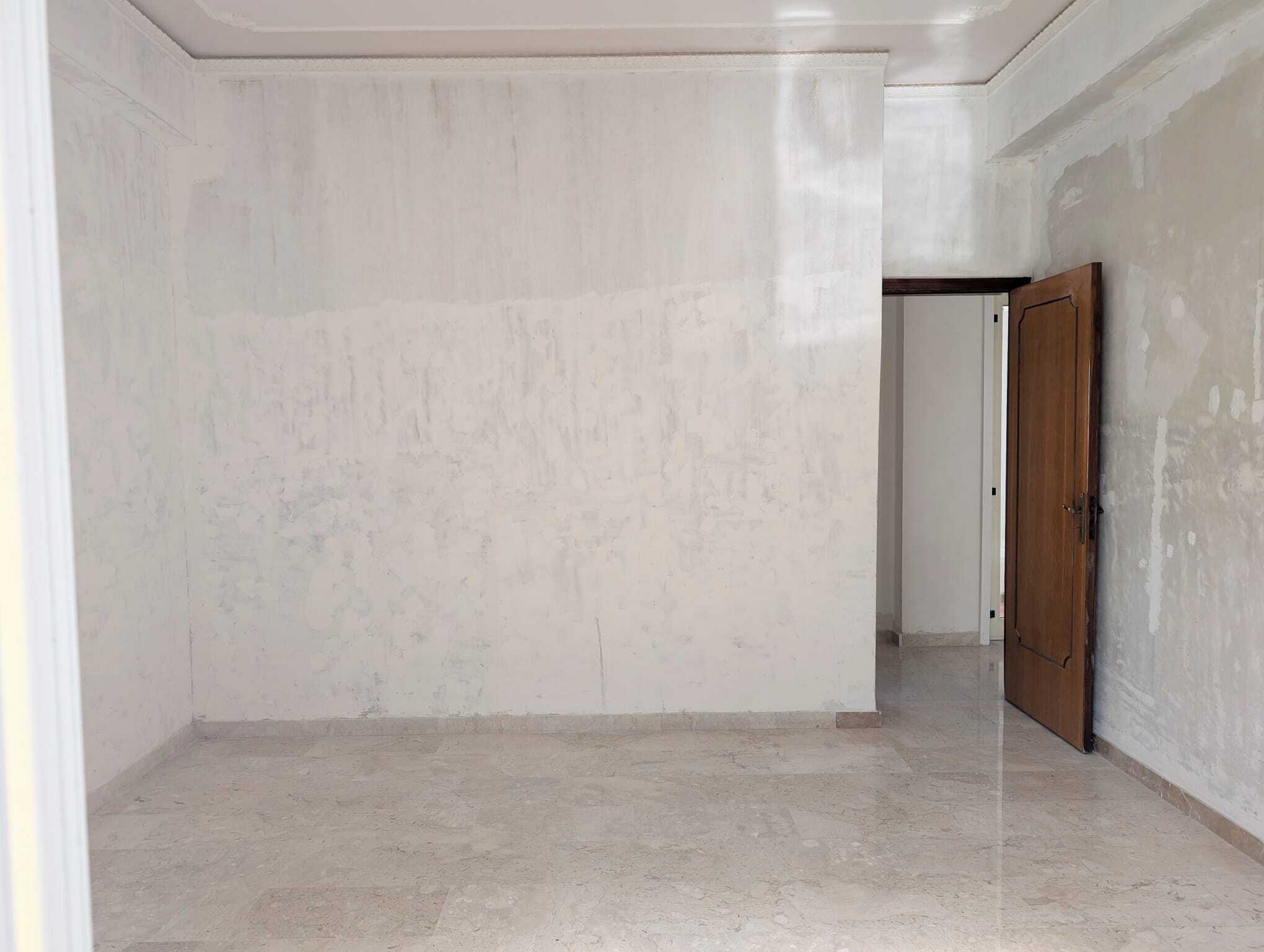 Spazio vuoto e luminoso in una stanza di casa con pareti e pavimenti chiari, porta in legno aperta, pronto per arredare o ristrutturare.