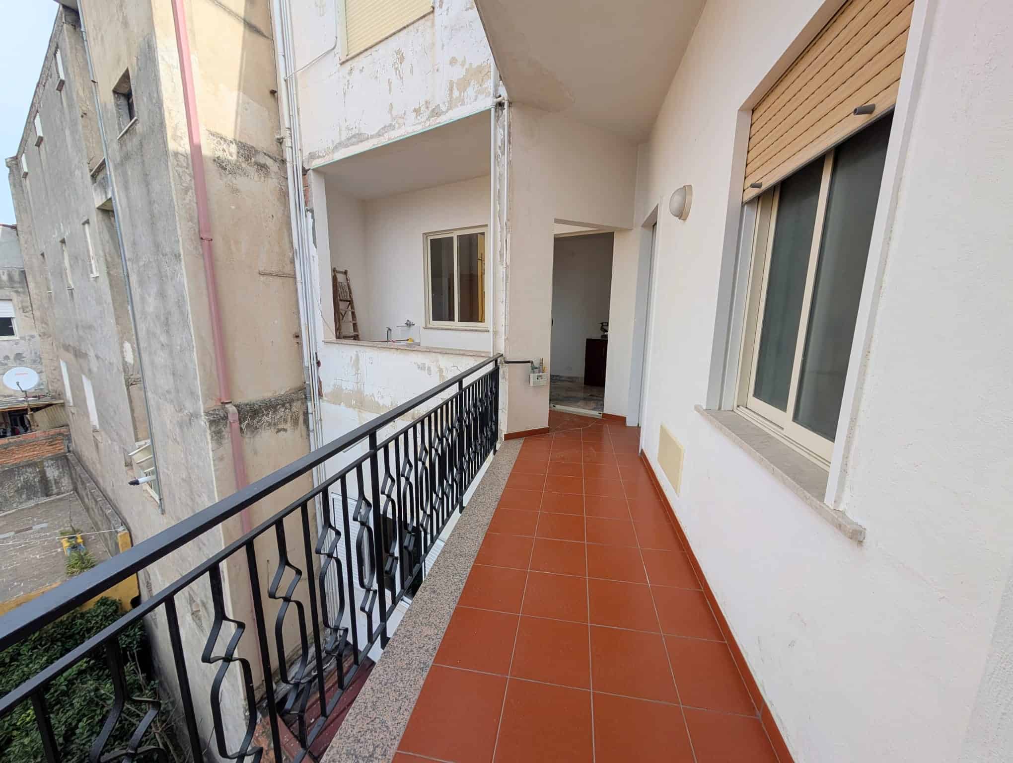 Balcone di un appartamento con ringhiera in ferro battuto, pavimento in piastrelle rosse e vista su edifici circostanti, ambiente luminoso e spazioso.