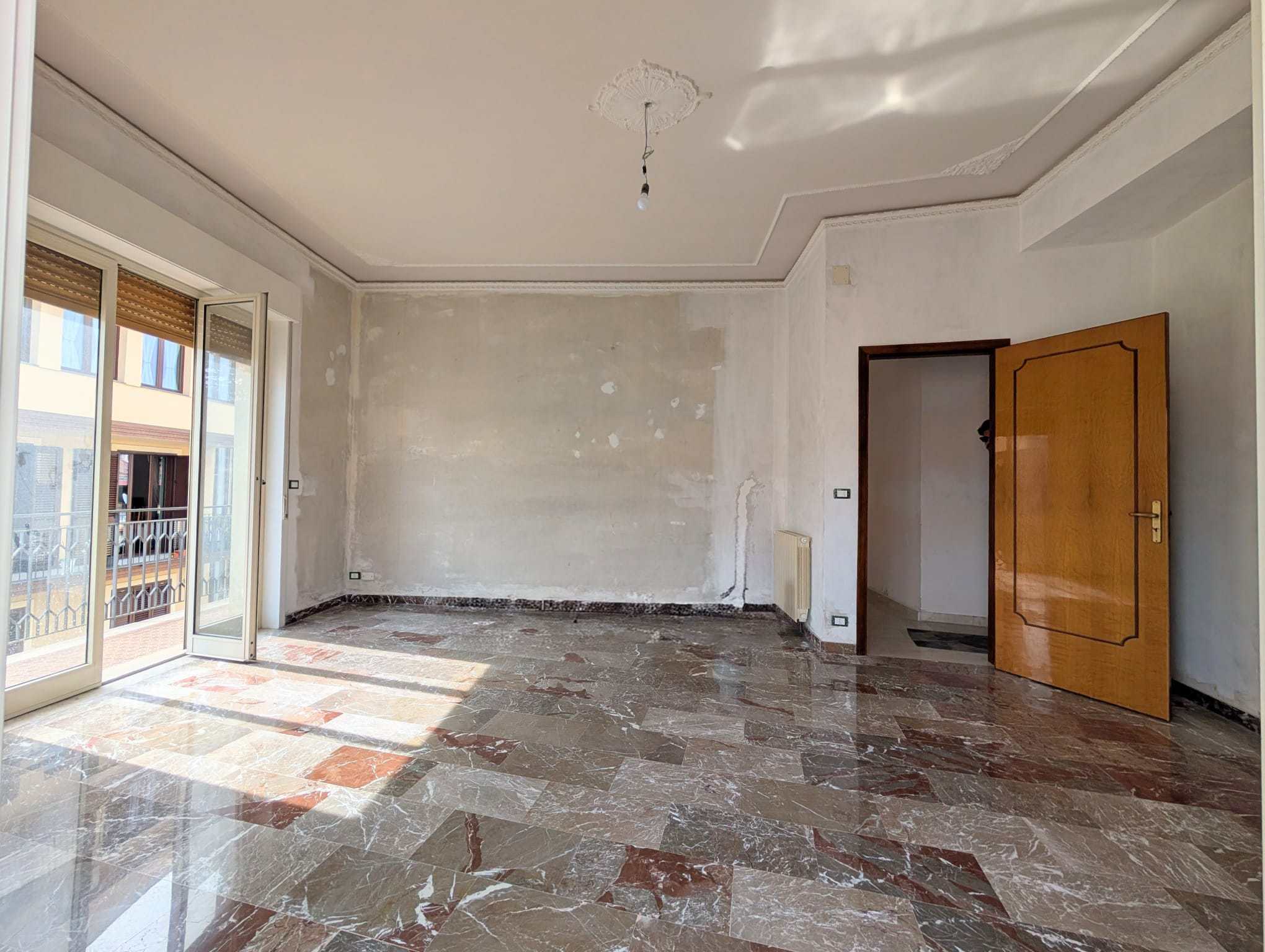 Appartamento vuoto in fase di ristrutturazione con pareti da dipingere, pavimento in marmo lucido e balcone con vista sulla città, pronto per essere personalizzato.