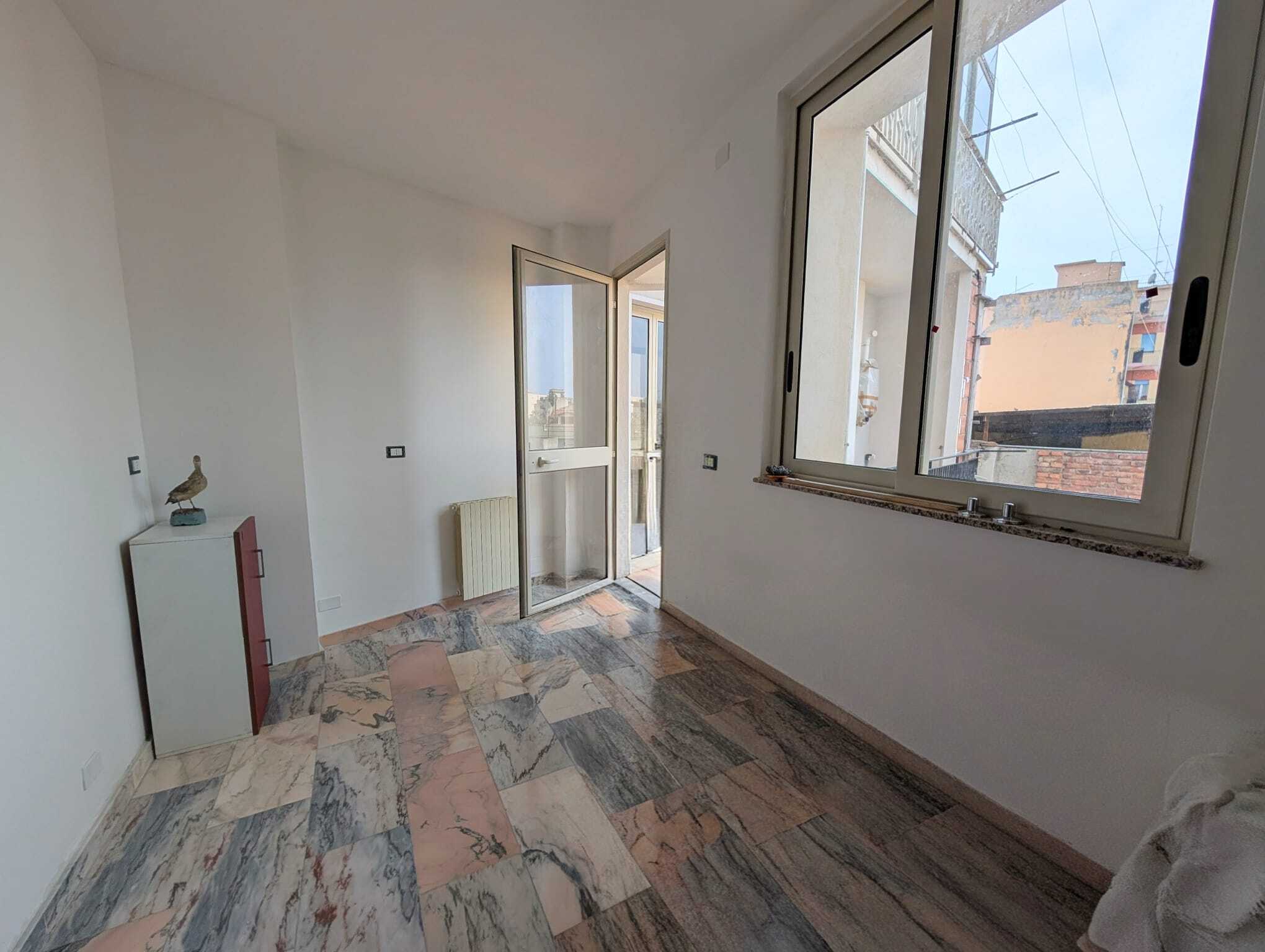 Appartamento luminoso con grandi finestre e balcone, ideale per vivere in città. Spazio interno con pavimento in marmo, pareti bianche e accessori minimalisti, perfetto per personalizzare gli ambienti.