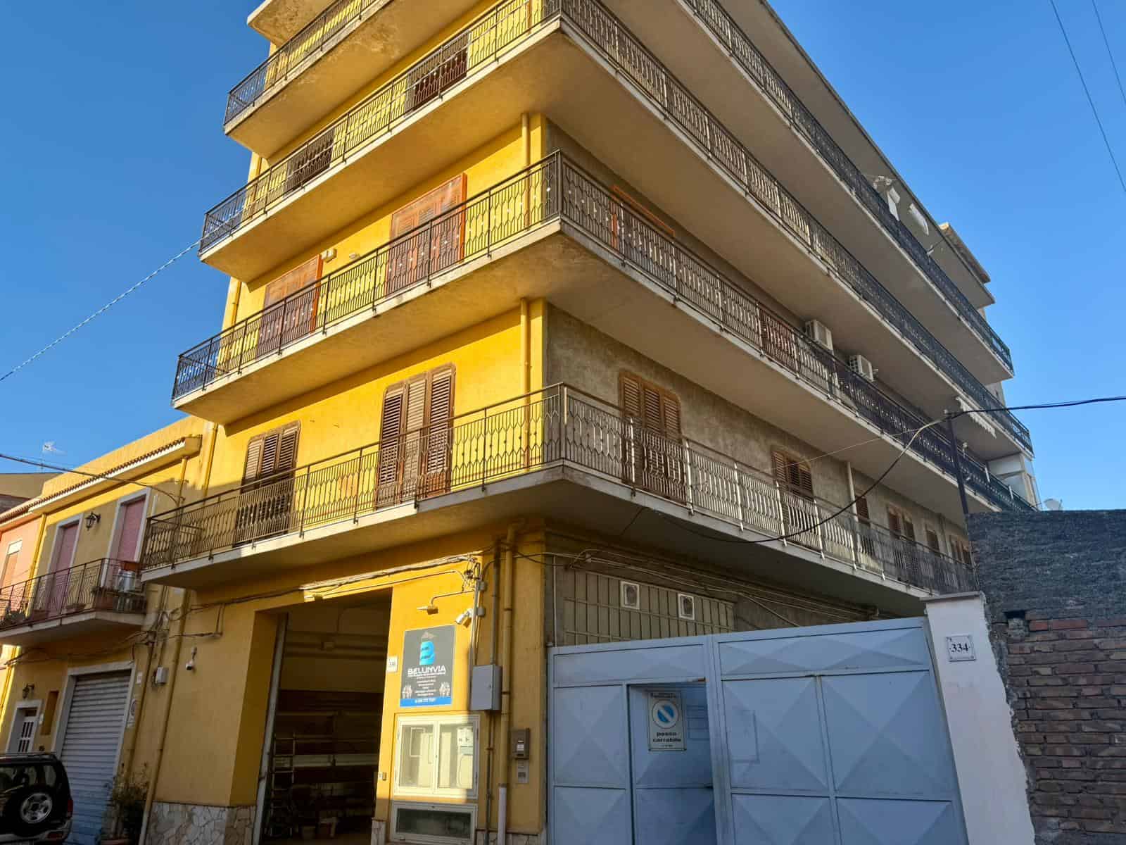 Appartamento in vendita in edificio giallo con balconi, situato in zona urbana, con accesso tramite cancello automatico e garage al piano terra. Ideale per investimento o residenza familiare.