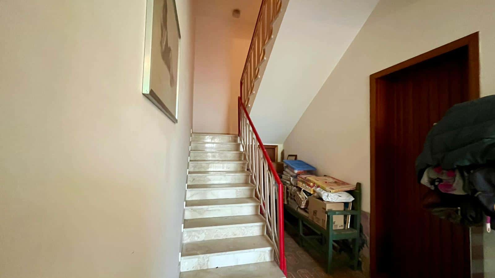 Scala interna in marmo con ringhiera rossa, vista dal basso, in un ambiente domestico luminoso e accogliente.